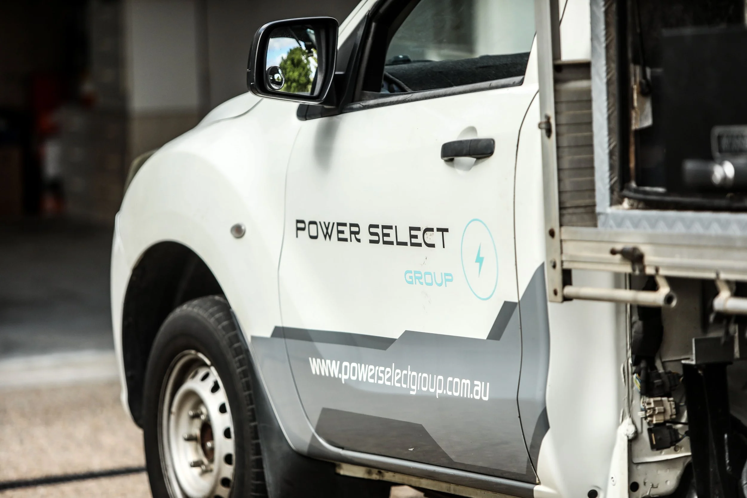 Close-up of a white electric utility vehicle with the logo and website of Power Select Group on the door, parked indoors.