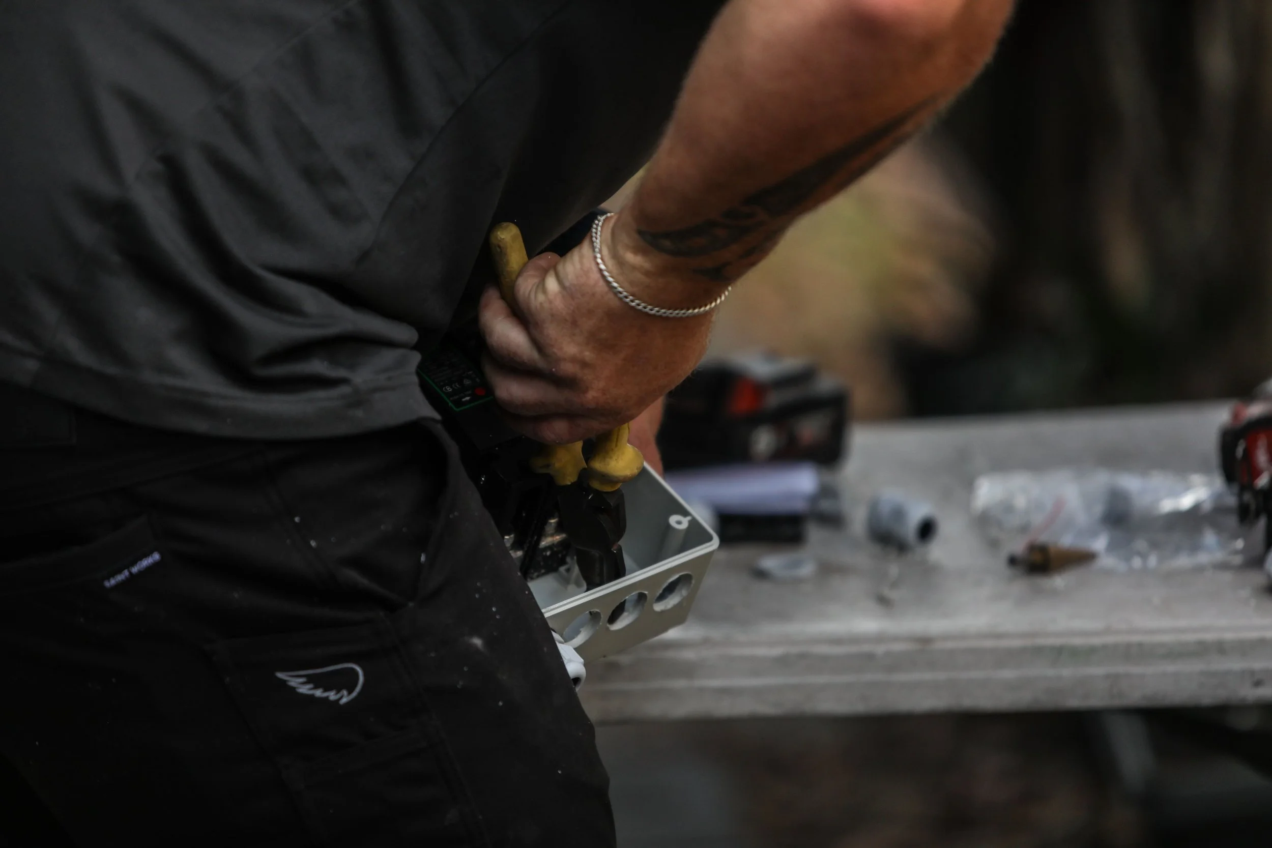 Close-up of a person working on a metal box, using a screwdriver, with tools and small parts on a work surface.