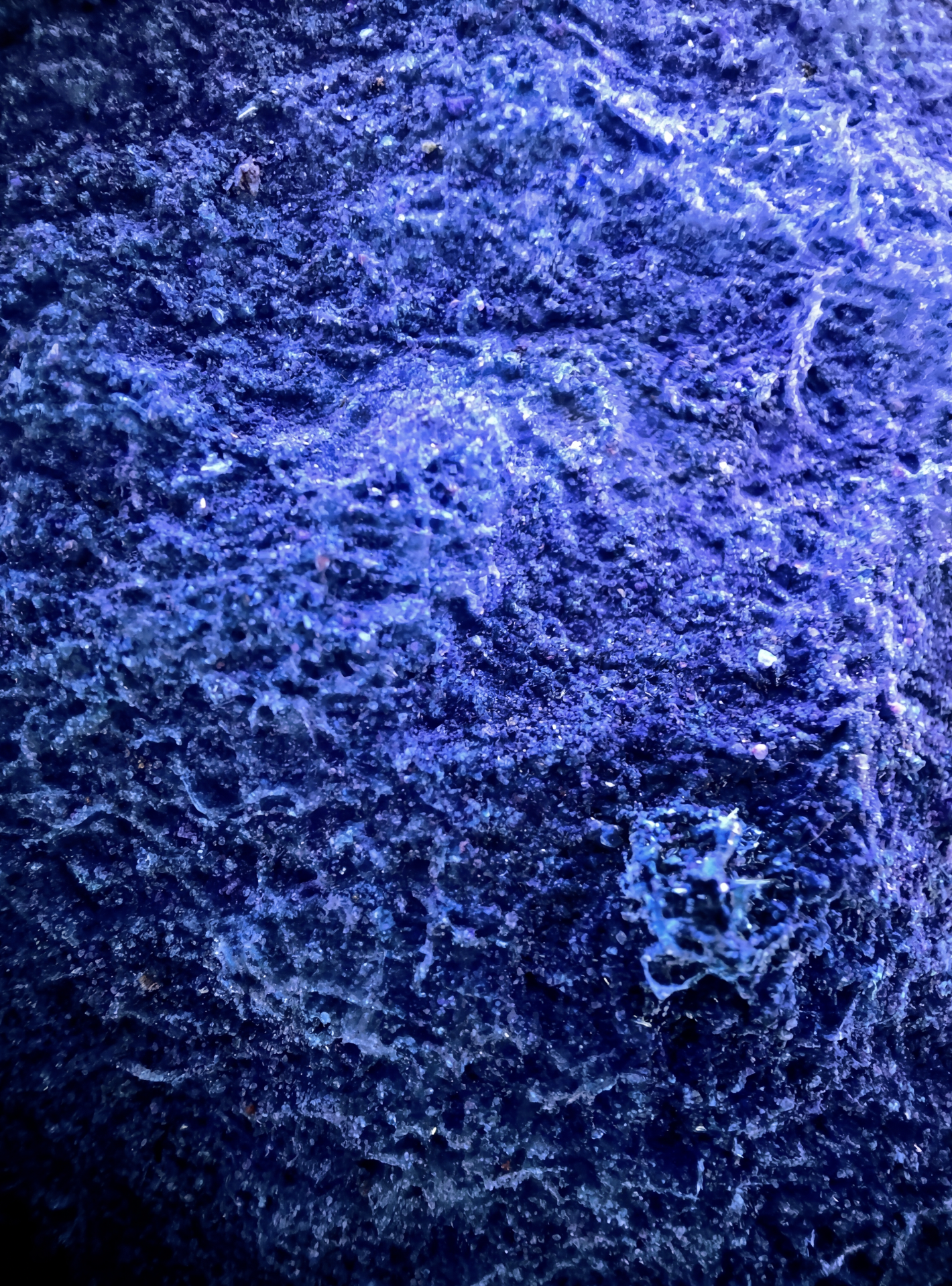 Surface rocheuse recouverte de cristaux brillants sous une lumière bleue.