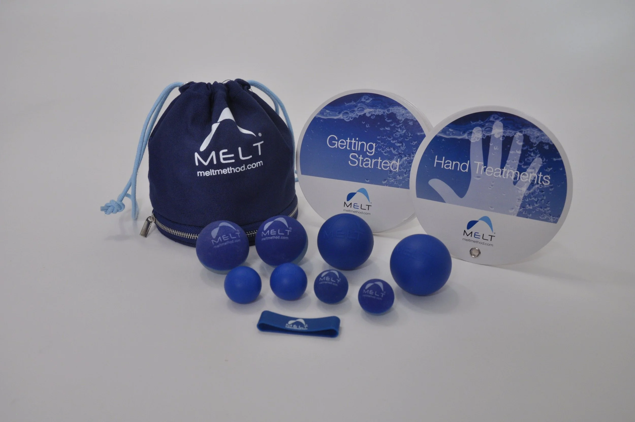 Set of blue MELT therapy balls of various sizes, a blue drawstring pouch with MELT logo, and two circular instructional signs labeled 'Getting Started' and 'Hand Treatments' on a white background.