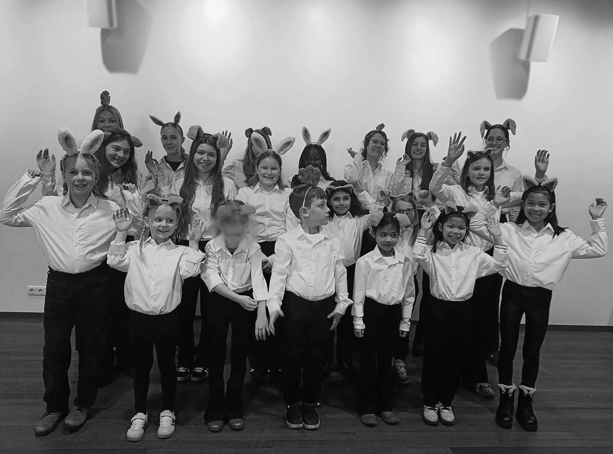 Een groep kinderen en volwassenen, gekleed in witte shirts en met bunny-oortjes, poseert voor een foto in een zaal.
