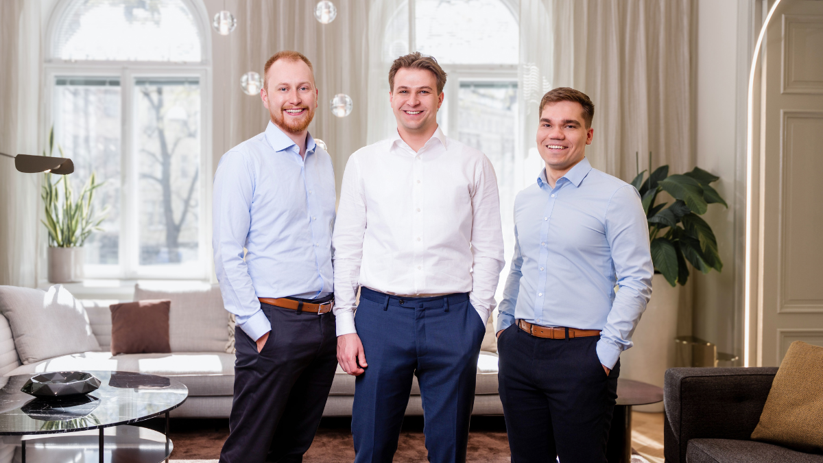 Three men standing and talking in a room with white walls covered in notes, labeled as part of a project or planning session.