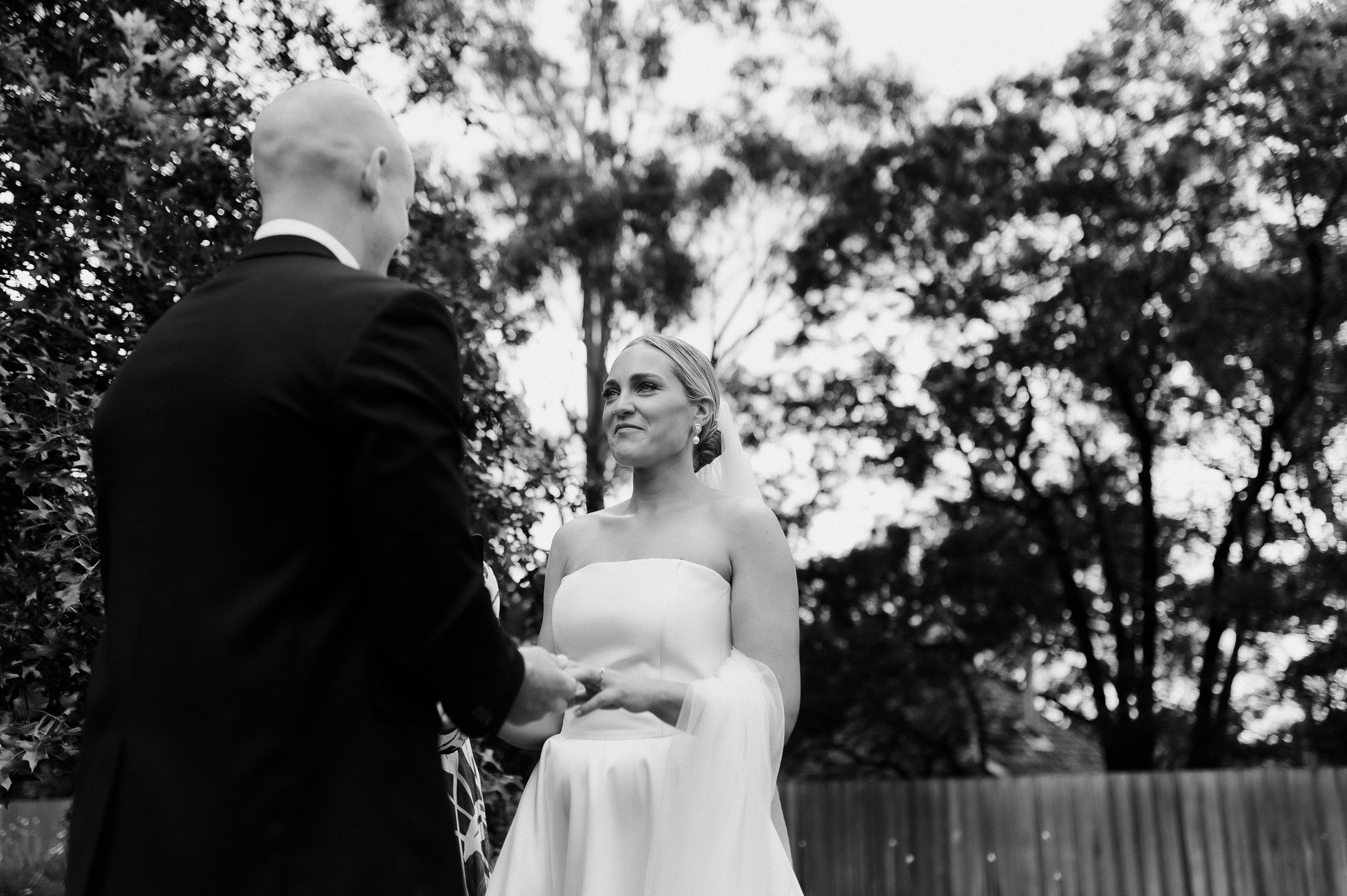 image shows a woman in a white dress, holding hands with a man in a suit. The man is facing away from the camera with the focus on the woman.