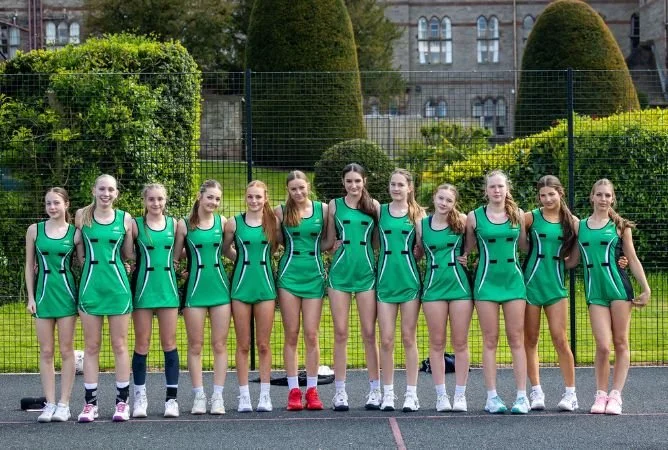 A girls' volleyball team standing on a court outdoors, wearing matching green uniforms and posing for a team photo.