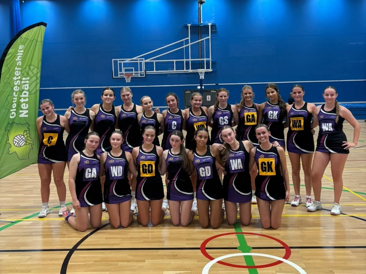 A girls' netball team in purple and black netball dresses, posing for a group photo in plock court.