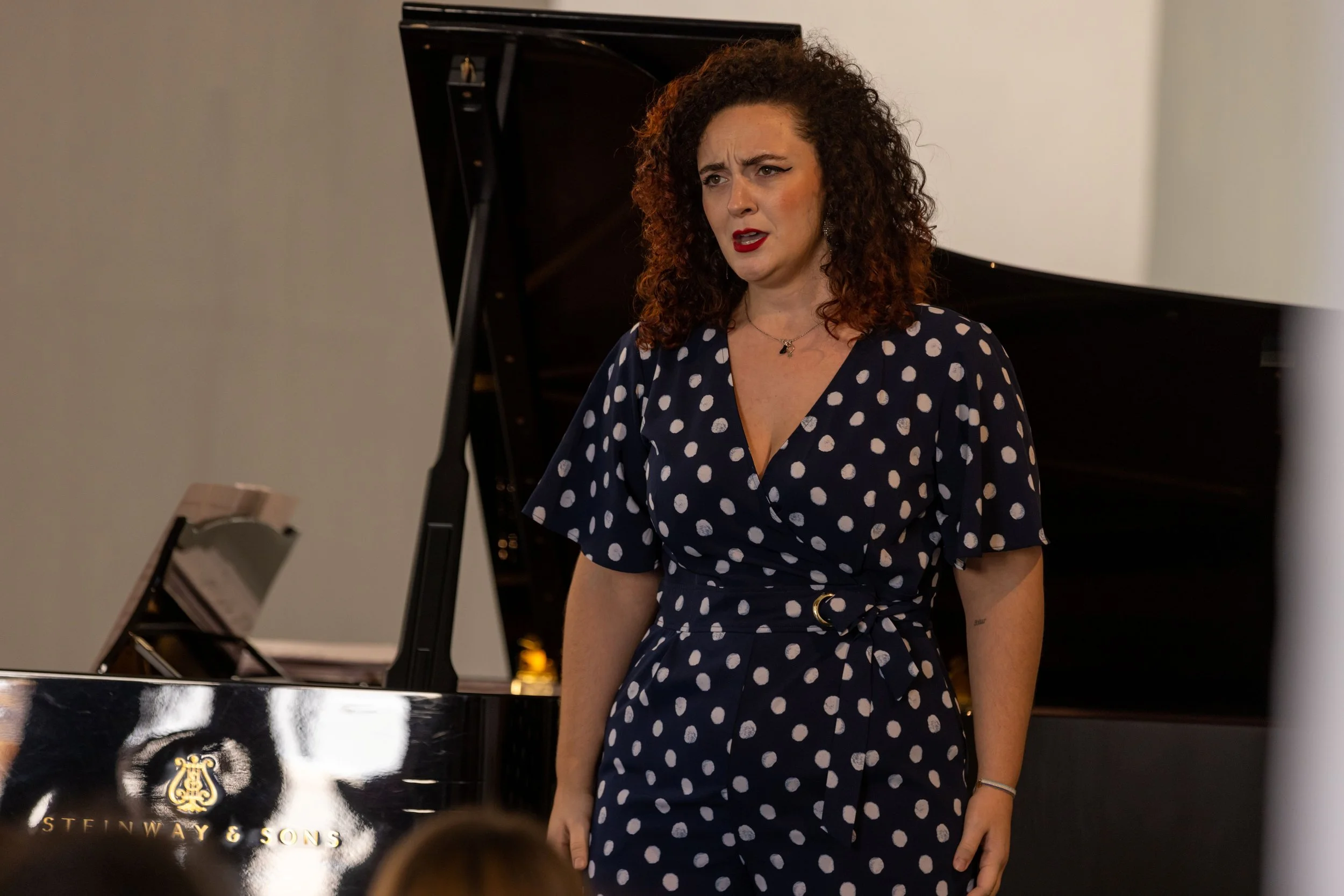 Mujer con vestido de lunares y cabello rizado delante de un piano Steinway en interiores.