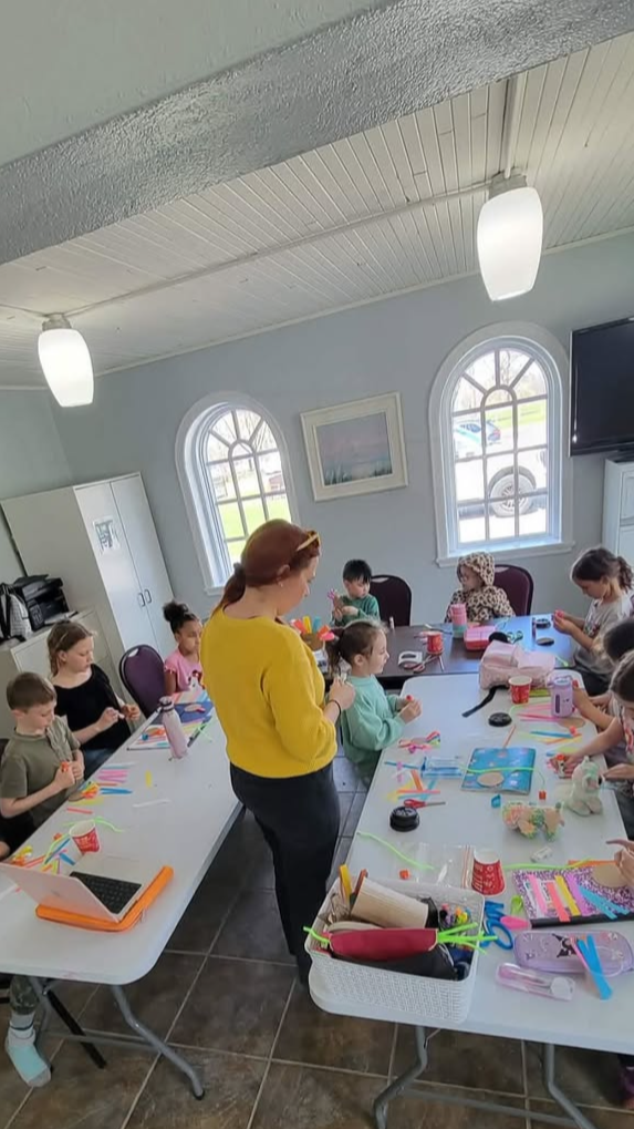 Groupe d'enfants et d'une femme dans une salle, participant à un atelier d'art ou de bricolage.