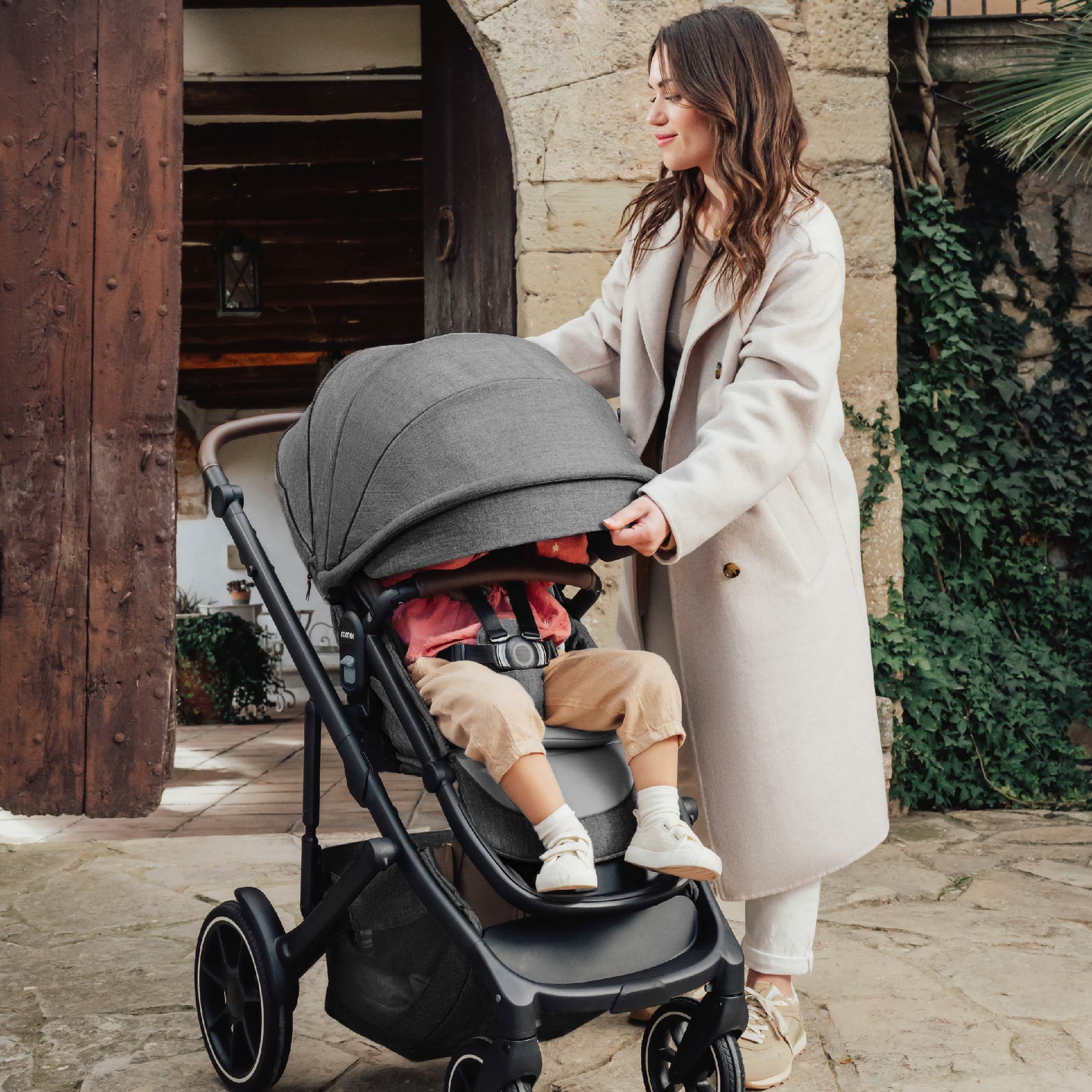 A woman pulling down the canopy on a toddler stroller.