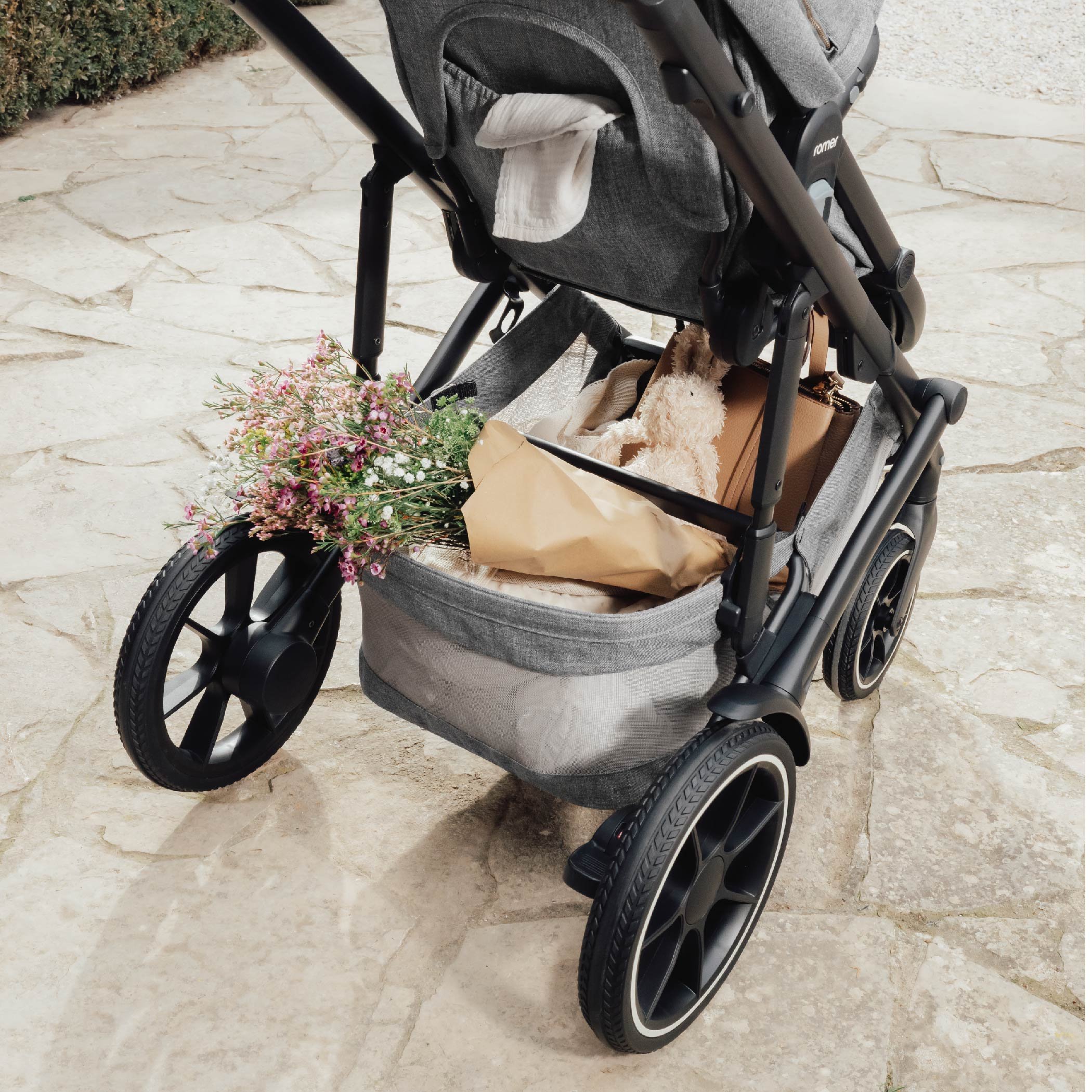 A stroller with flowers, a stuffed animal, and other items in the storage basket.