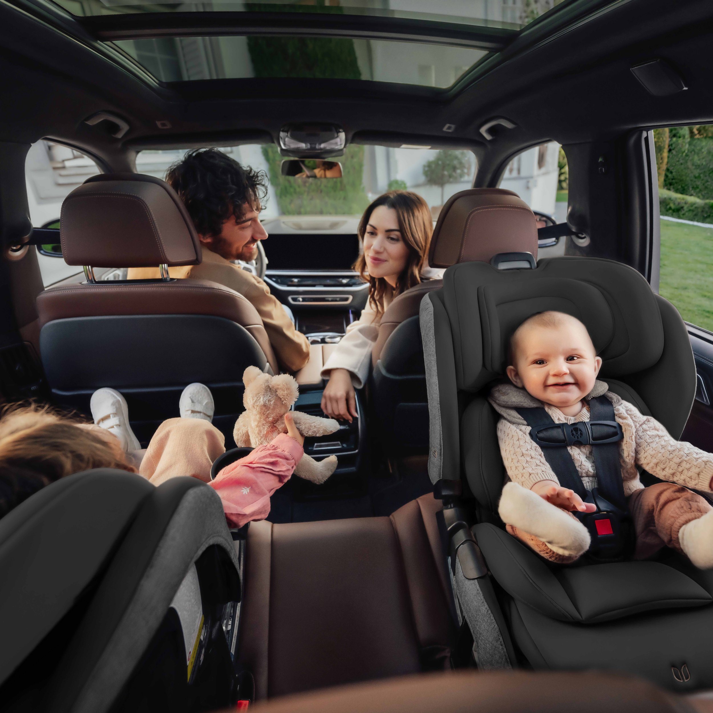 A man and a woman in a vehicle with a toddler and a baby in car seats.