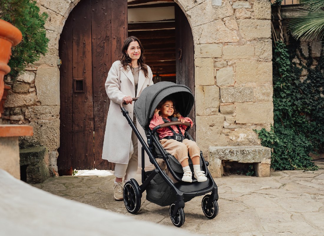 A toddler in a stroller with a canopy and a bumper bar.