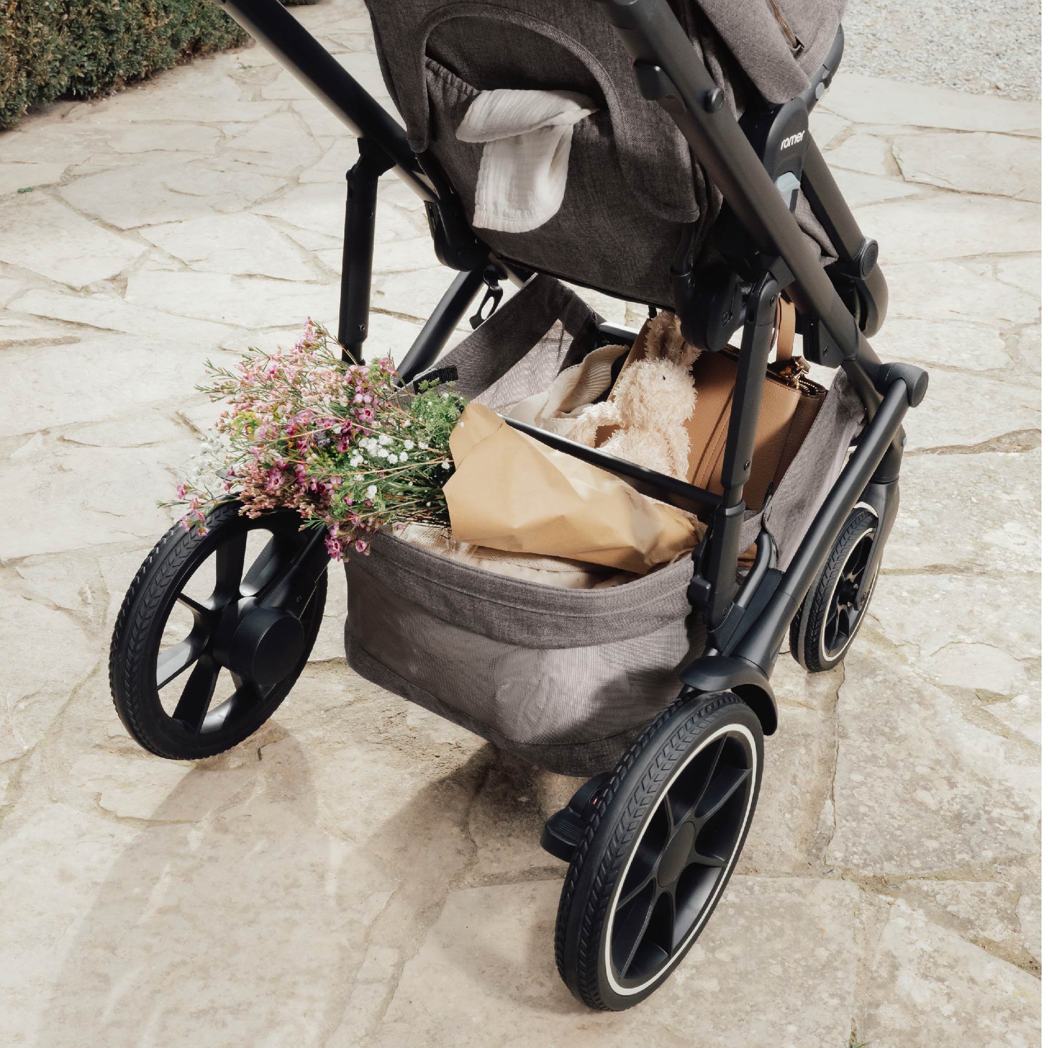 A stroller with flowers, a stuffed animal, and other items in the storage basket.