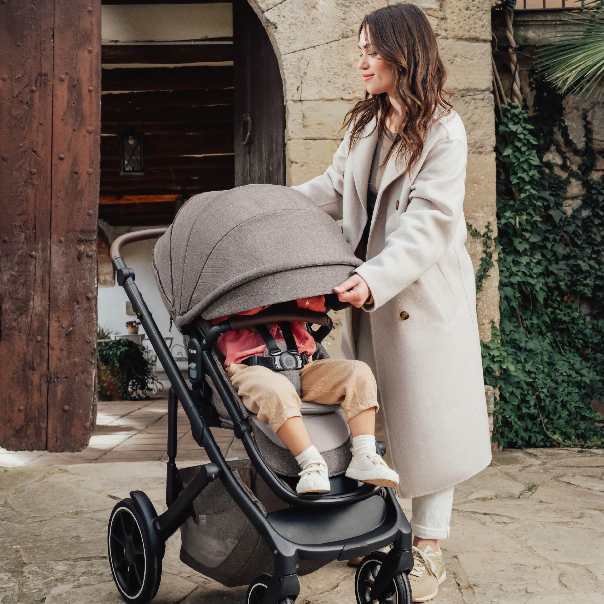 A woman pulling down the canopy on a toddler stroller.