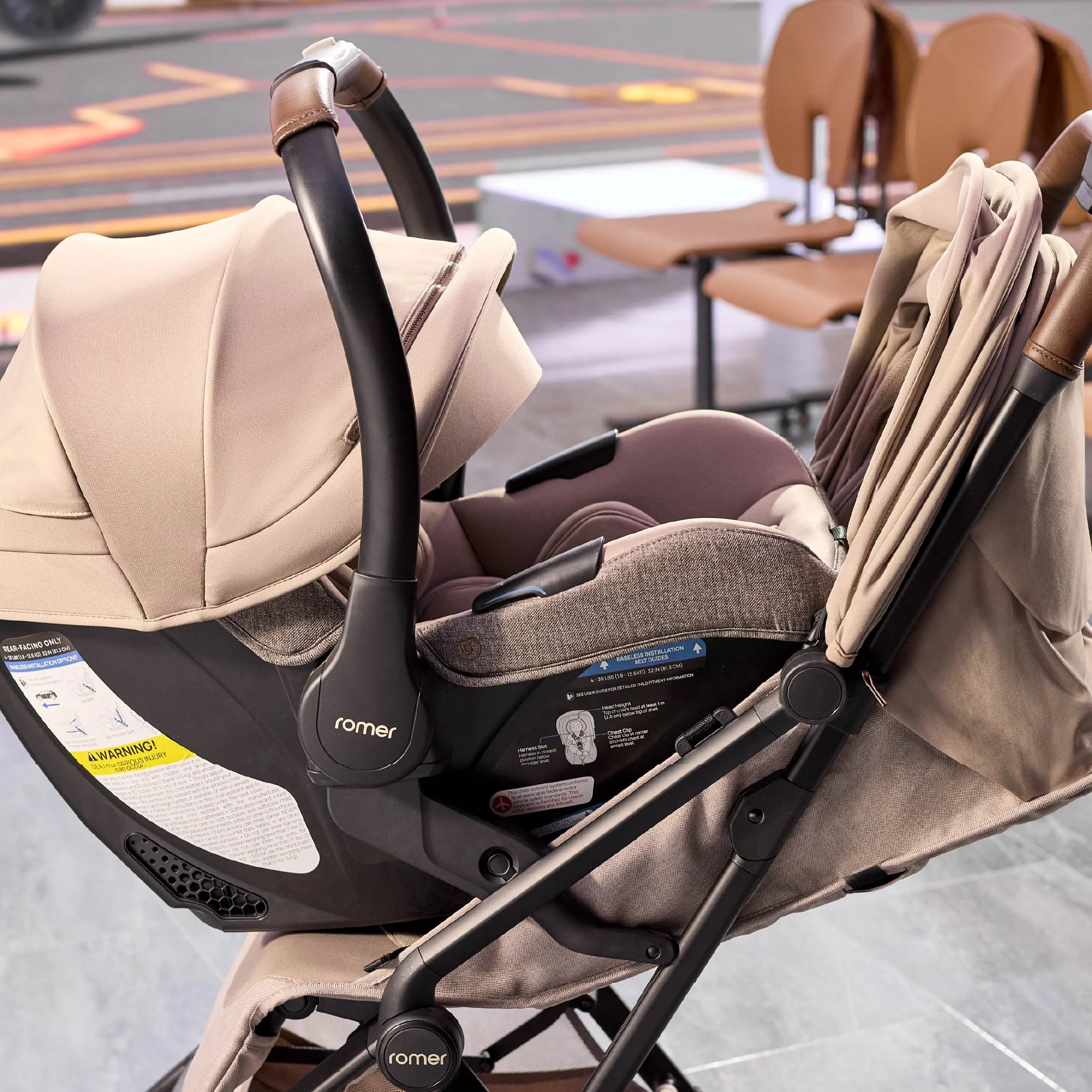 A tan infant car seat is securely attached to a matching stroller frame indoors. (Copy)