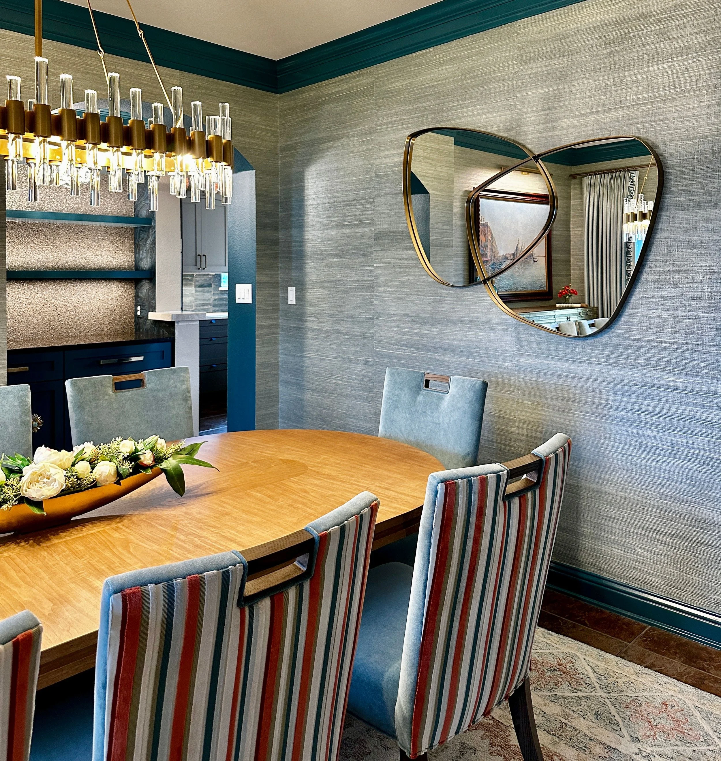This dining room at the Schug Cove project blends custom furnishings, sculptural lighting, and textured wallcovering to create a refined entertaining space with depth and personality. Cyndi Hopkins Design layered rich blue tones, tailored seating, an