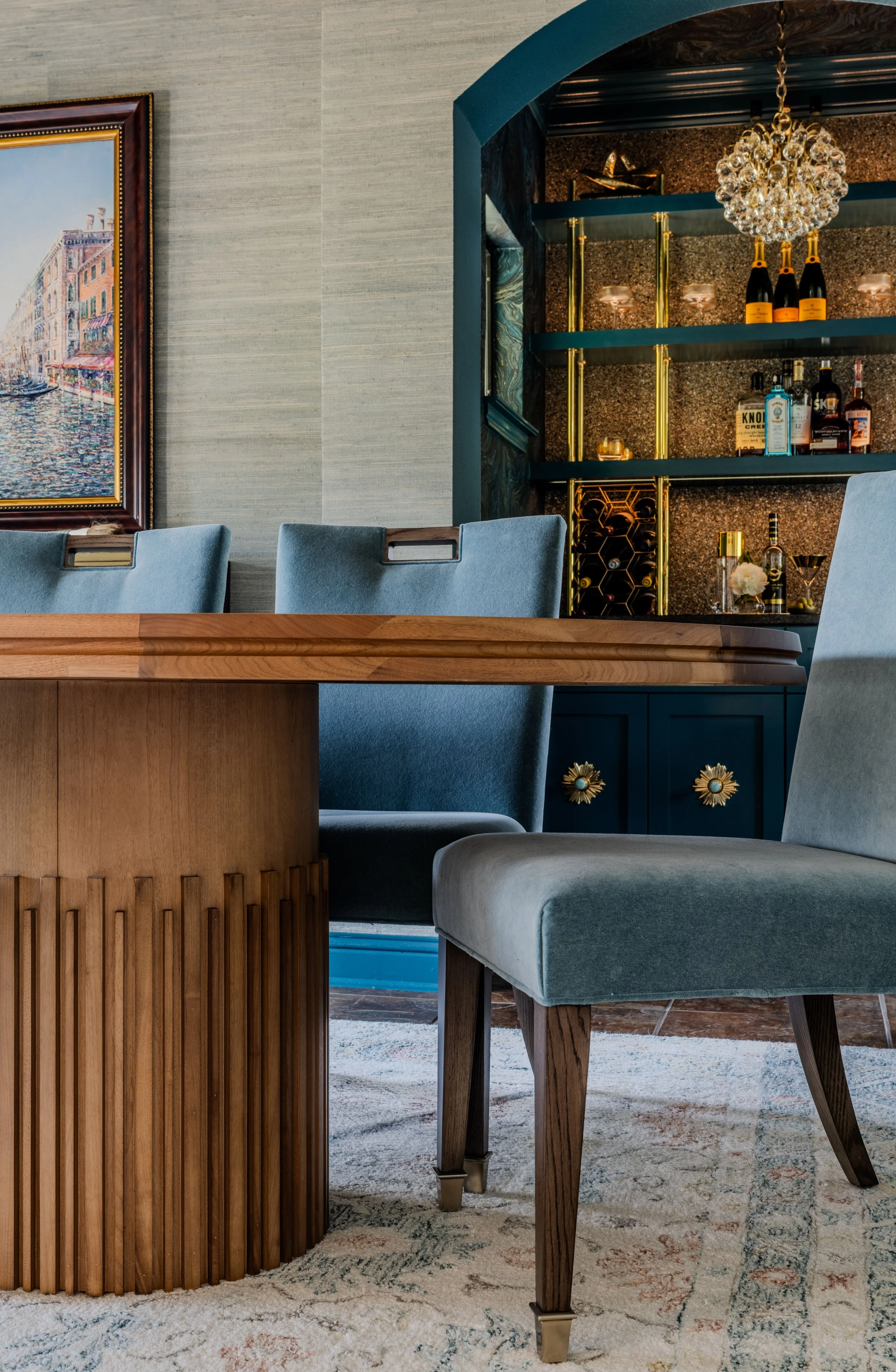 This luxury dining room at the Schug Cove project blends sculptural furniture, layered textures, and a dramatic custom wine bar to create an elevated entertaining experience. Cyndi Hopkins Design paired a custom fluted wood dining table with tailored