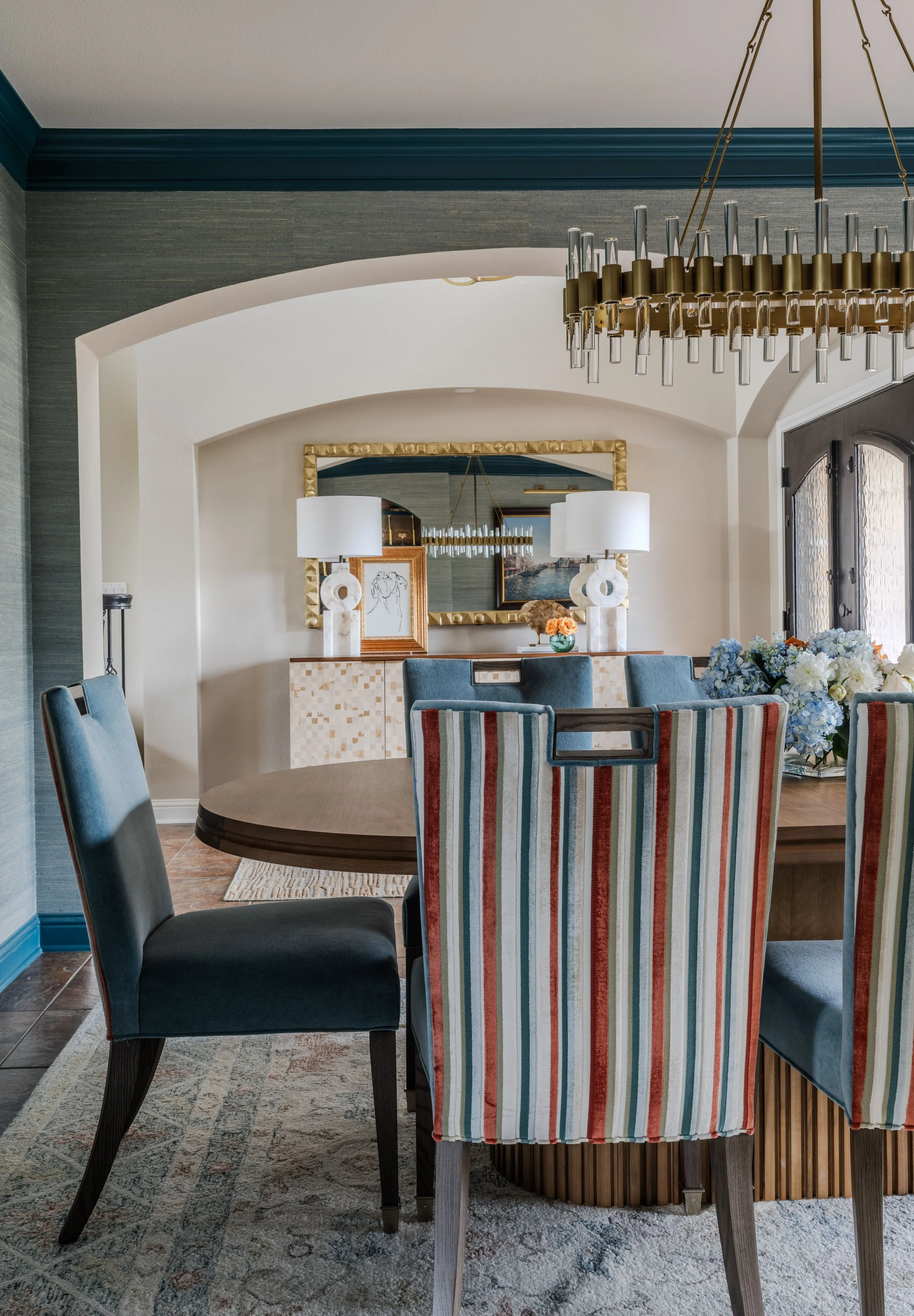 This dining room at the Schug Cove project layers custom dining chairs, sculptural lighting, textured wallcovering, and tailored furnishings to create a sophisticated entertaining space with warmth and personality. Cyndi Hopkins Design blended rich b