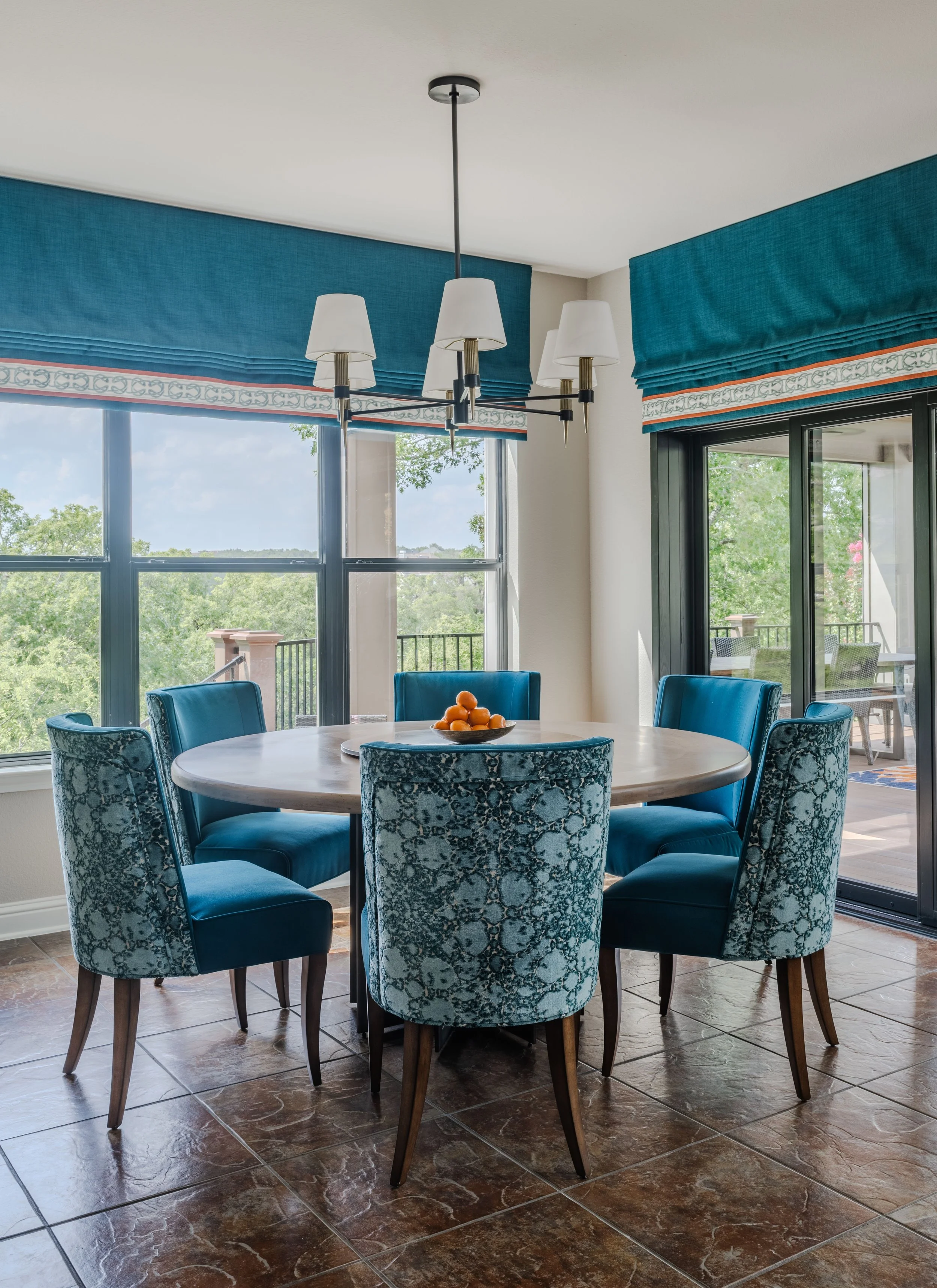 This breakfast room at the Schug Cove project combines custom dining chairs, tailored Roman shades, and layered blue tones to create a bright and welcoming gathering space. Cyndi Hopkins Design balanced vibrant color, natural light, and refined furni