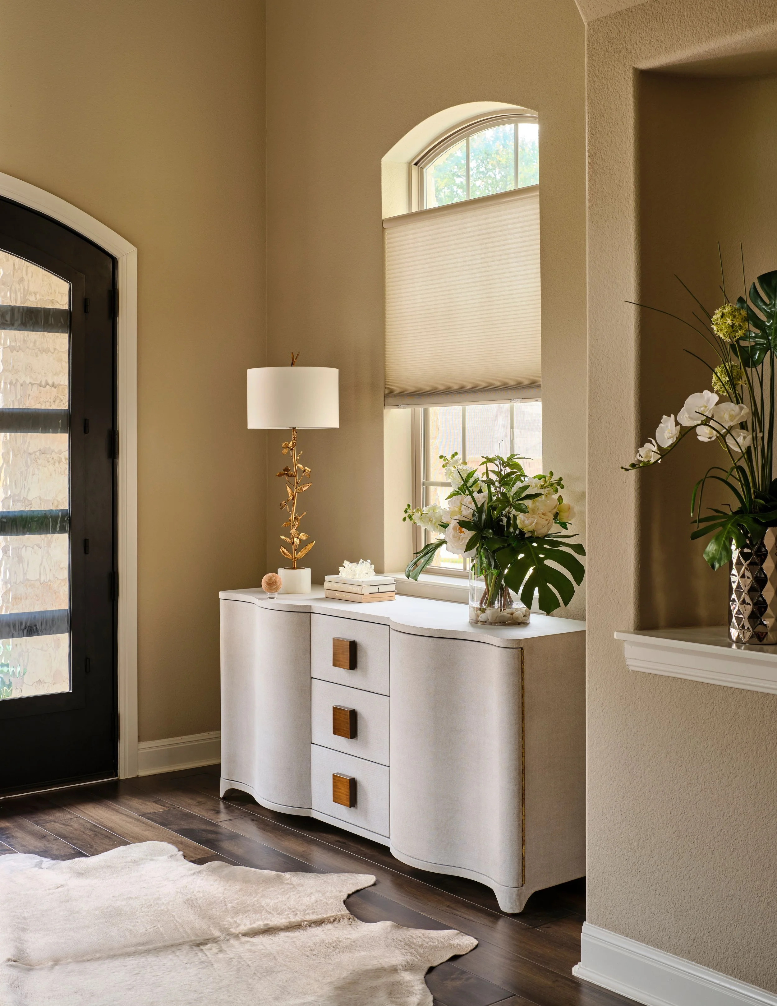 This foyer vignette pairs a custom console with tailored window treatments and layered styling to create a warm and welcoming entry. The mix of materials and natural light sets the tone for the home while maintaining a sense of ease and comfort.