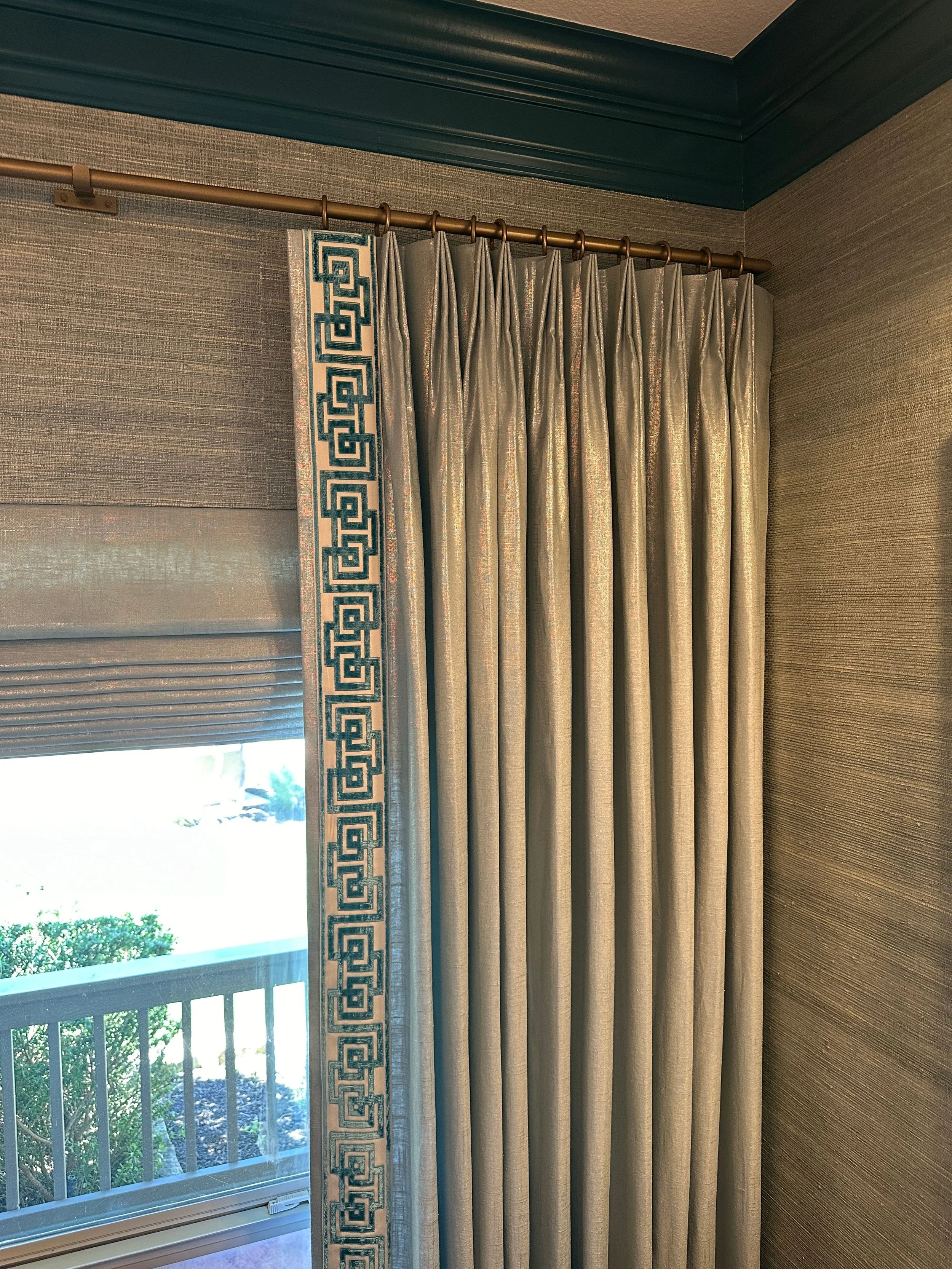 Custom window treatments at the Schug Cove project feature tailored drapery panels with bold Greek key trim layered against textured grasscloth wallcovering for a refined and collected look. Designed by Cyndi Hopkins Design, the soft neutral fabric, 