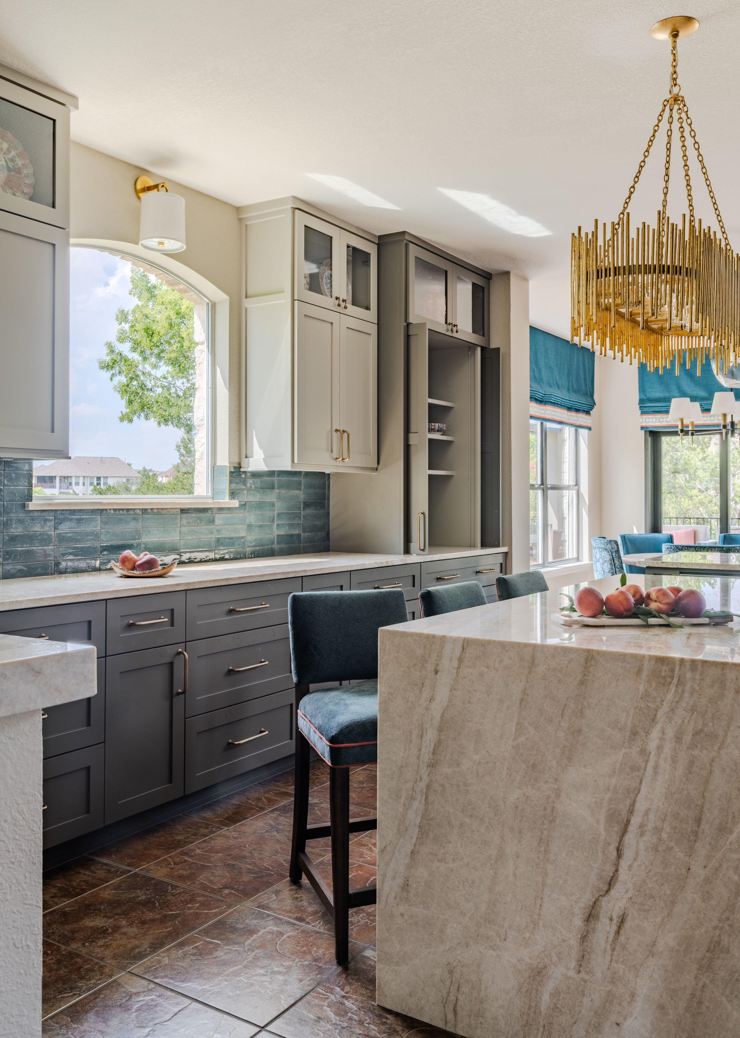 This kitchen at the Schug Cove project pairs a dramatic quartzite waterfall island with custom cabinetry, layered storage, and rich blue tile accents to create a refined yet highly functional gathering space. Cyndi Hopkins Design balanced warm materi