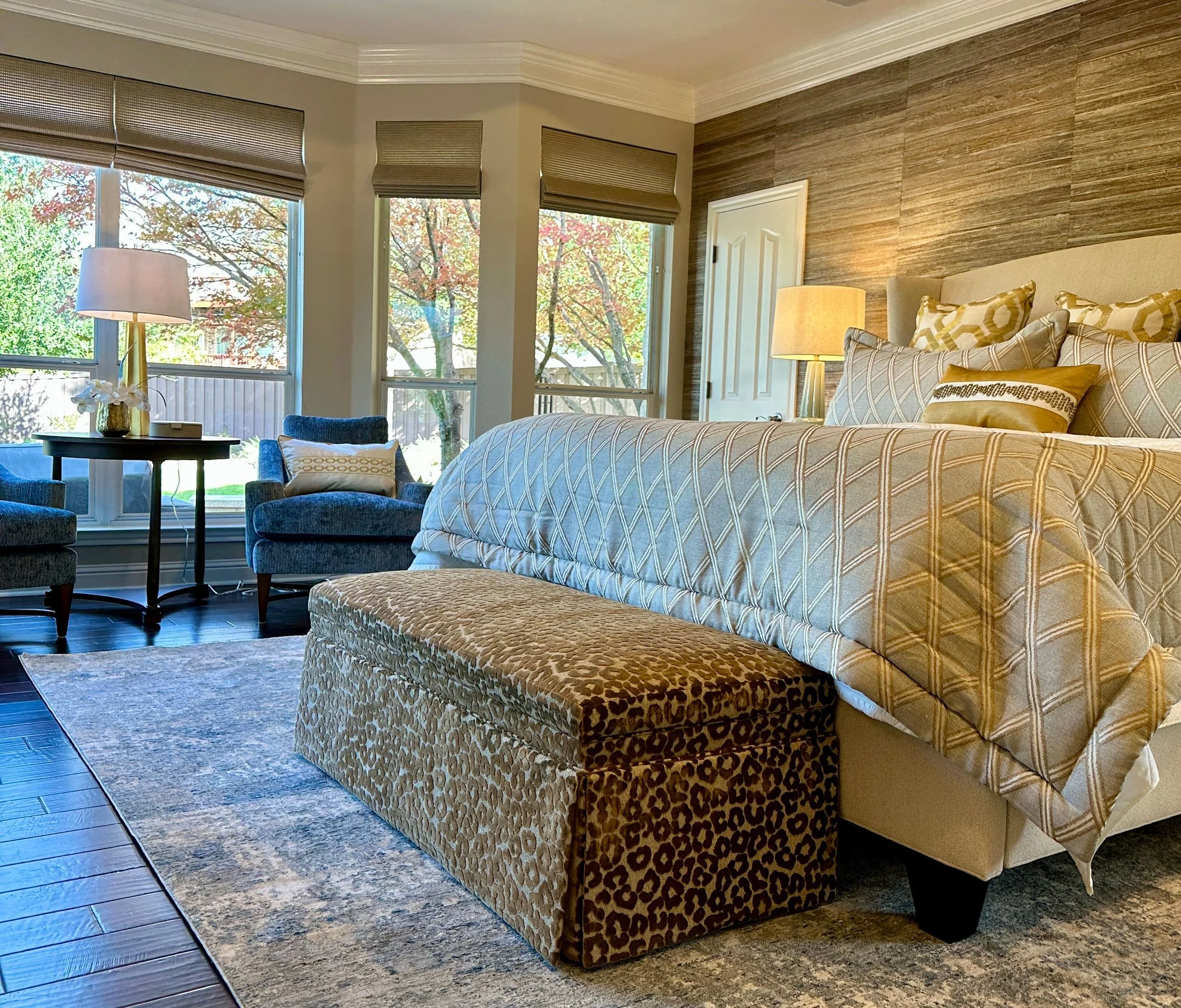 This serene primary bedroom at the Schug Cove project was designed by Cyndi Hopkins Design to feel warm, tailored, and deeply inviting. The luxury Austin Texas bedroom features custom bedding, textured grasscloth wallcovering, sculptural lighting, la