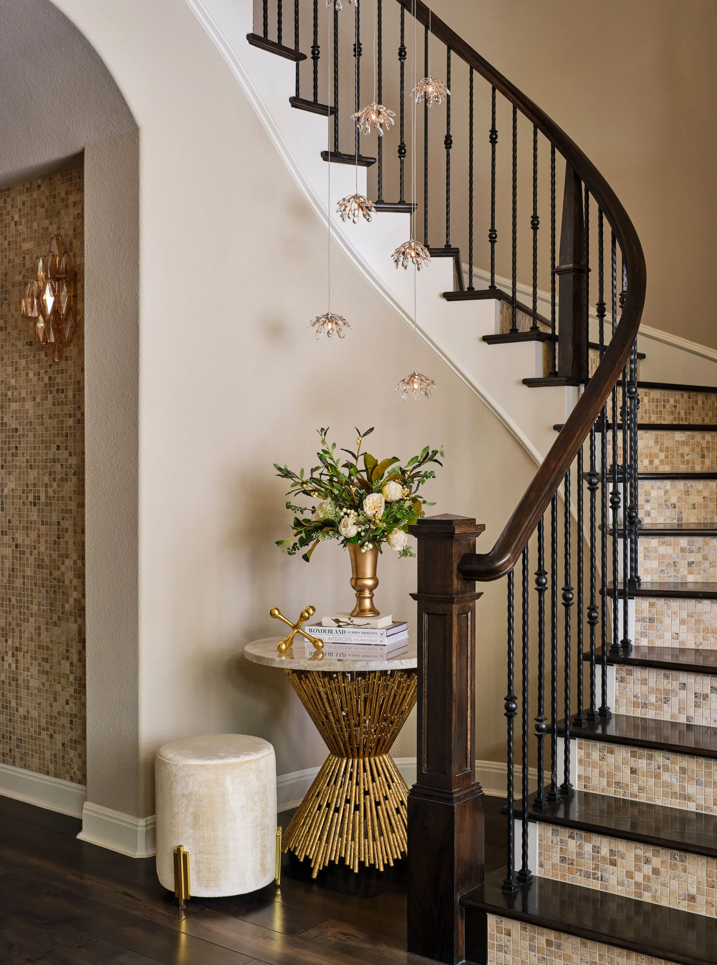 This staircase and entry moment highlights the importance of thoughtful lighting and architectural detail. Pendant lighting adds softness and movement, while the curved stair and iron railing bring structure and balance to the space.