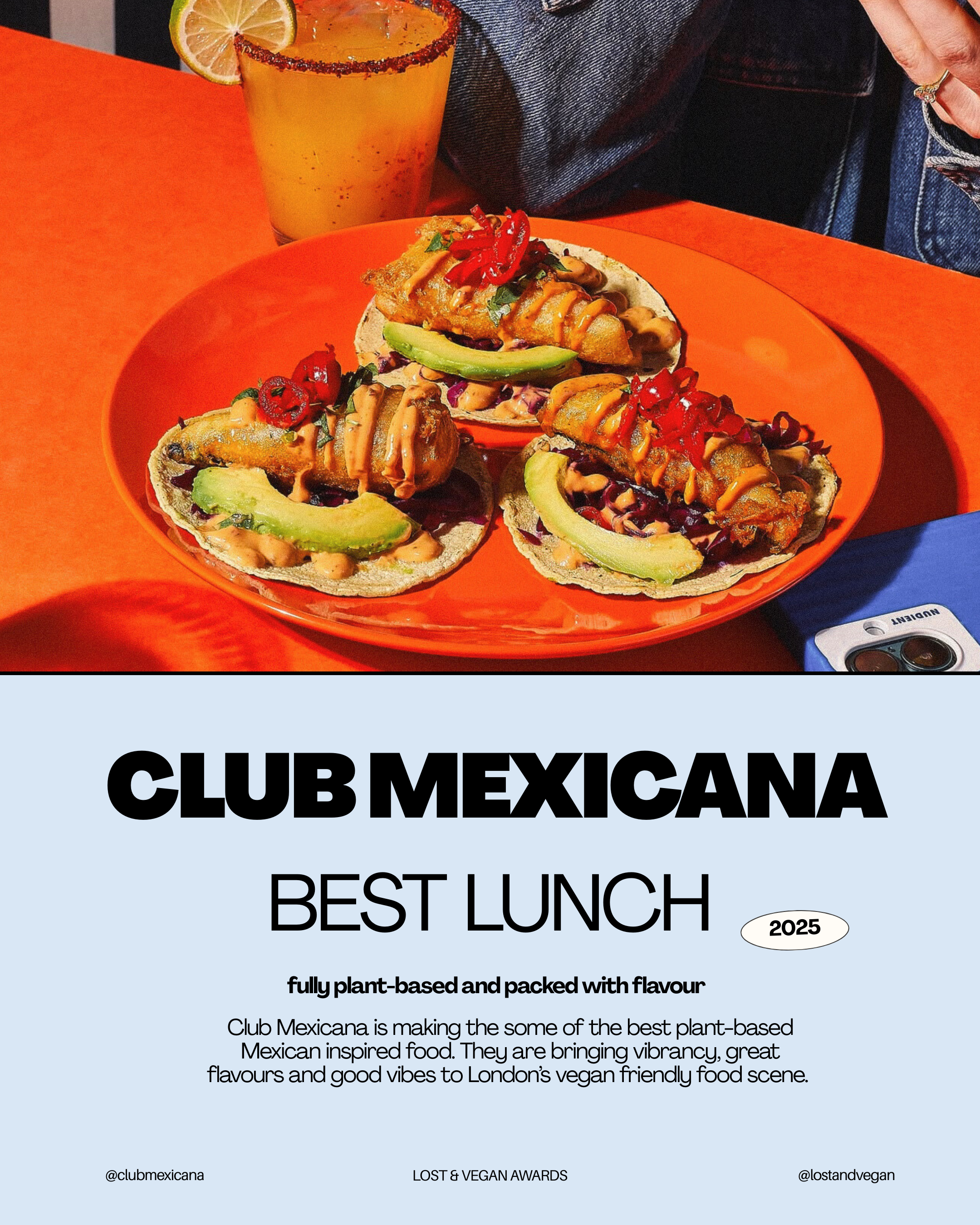 A plate of three vegan Mexican-style tacos with avocado slices, red chili peppers, and drizzled sauces on corn tortillas, topped with crispy battered filling, accompanied by a glass of orange-colored beverage with a lemon slice, all set on an orange table.