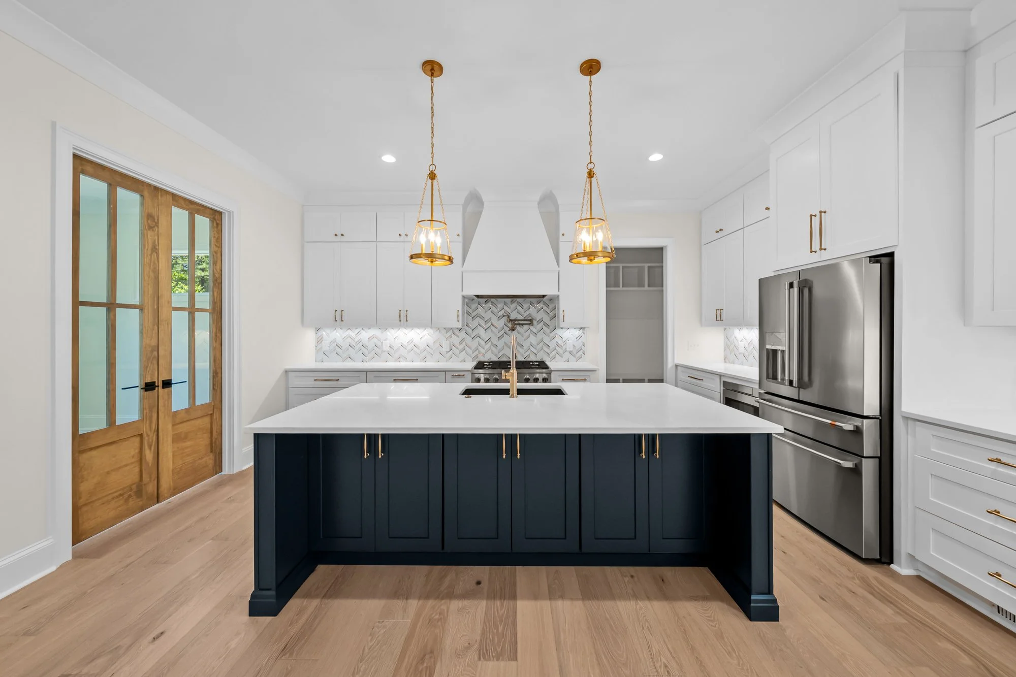 Custom kitchen by FRS Homes featuring a navy blue island, white shaker cabinetry, quartz countertops, designer lighting, and premium appliances.