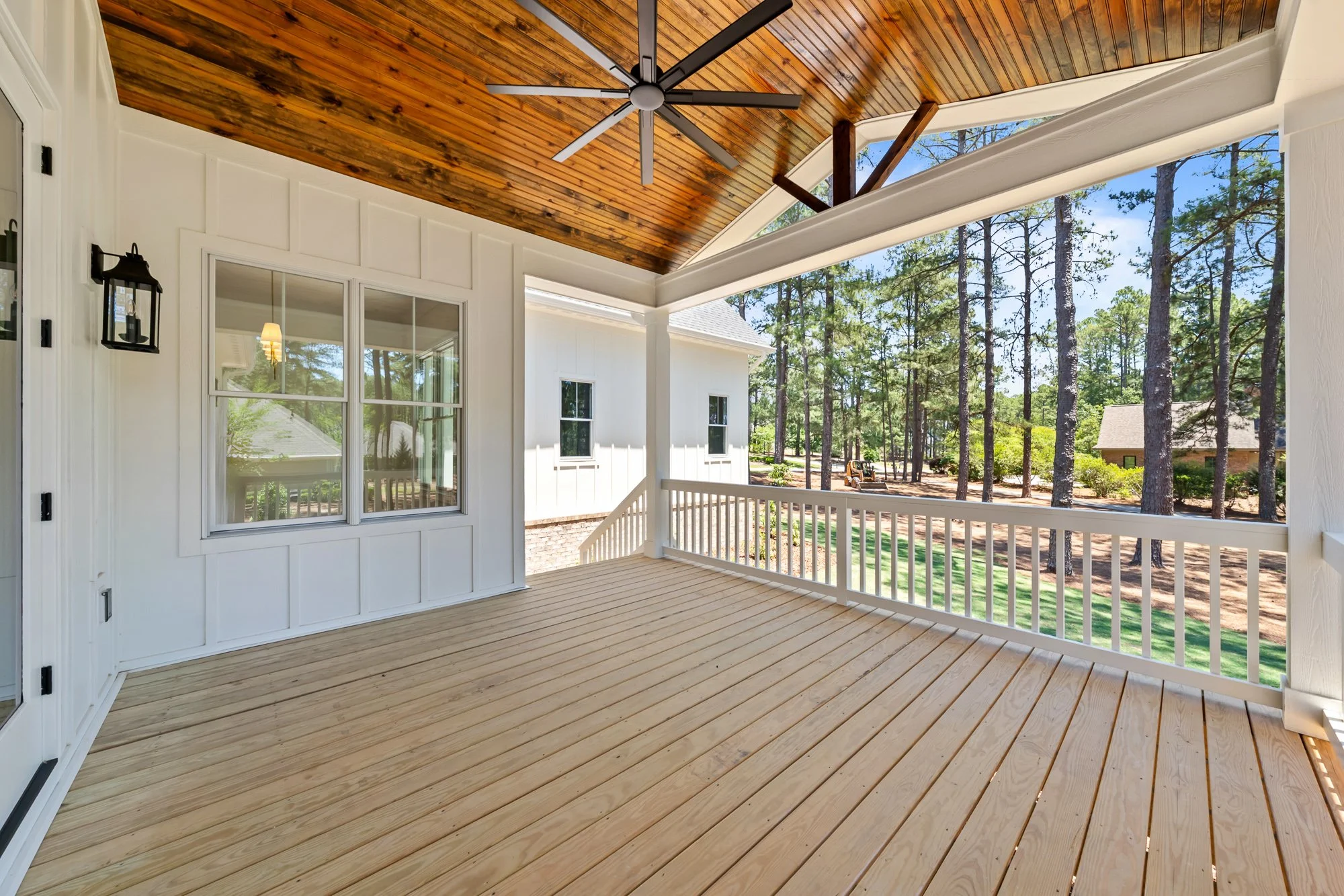 Covered outdoor living porch by FRS Homes featuring a vaulted stained wood ceiling, oversized ceiling fan, and peaceful wooded views.