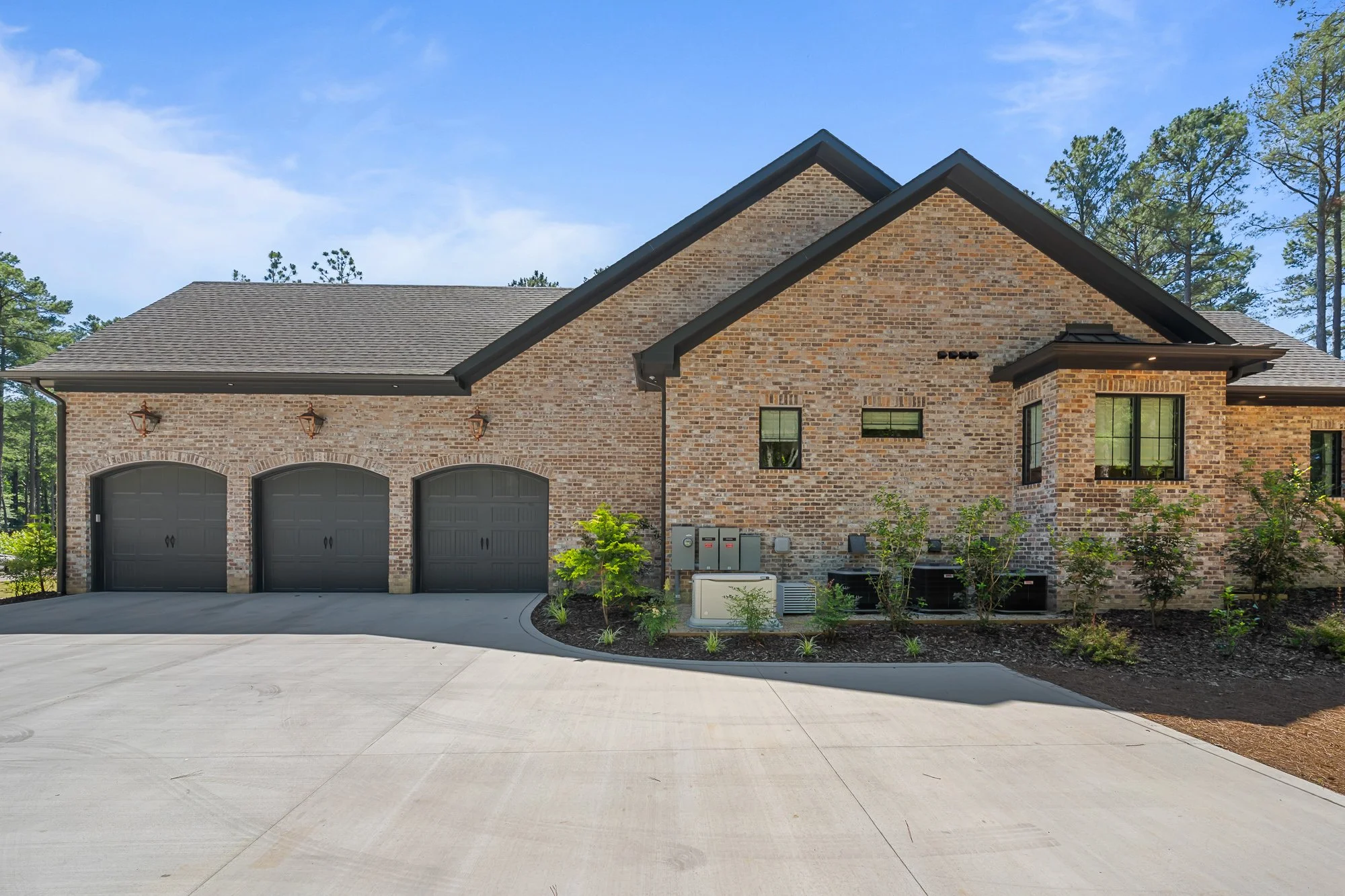 Side elevation of a luxury custom brick home by FRS Homes featuring a three-car garage, steep gabled rooflines, black carriage-style garage doors, and European-inspired architectural details in Southern Pines, NC.
