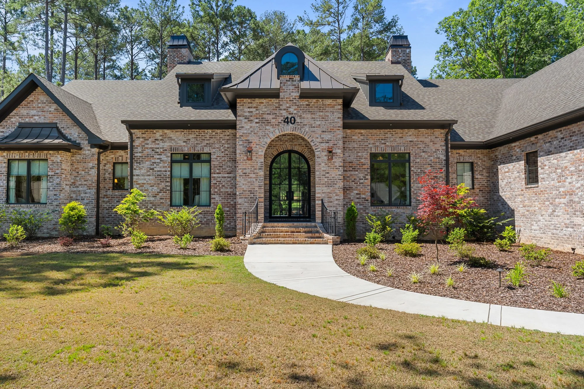 Luxury custom brick home by FRS Homes featuring European-inspired architecture with arched black steel entry door, painted brick exterior, steep gables, and professionally landscaped front yard in Southern Pines, NC.