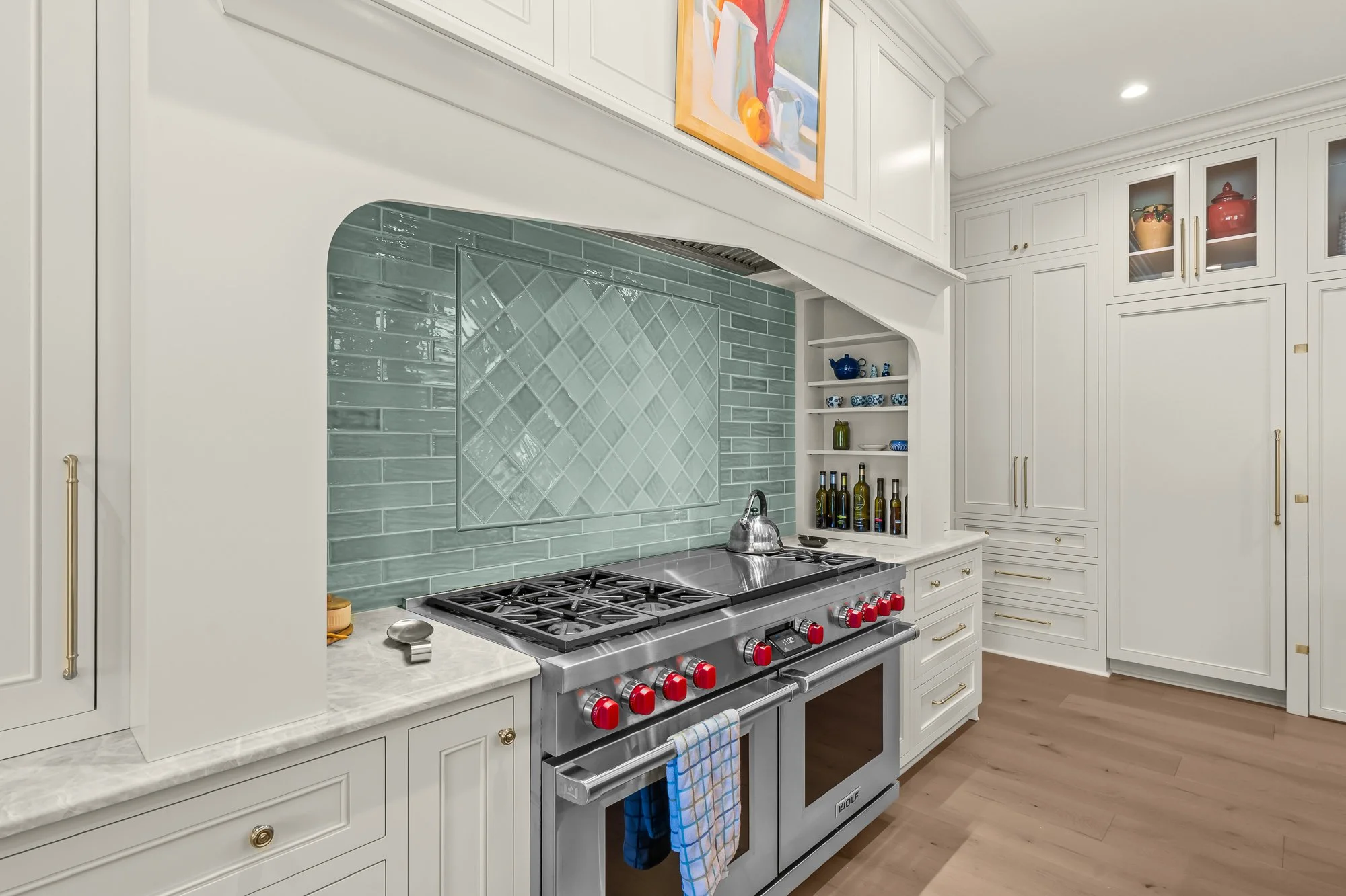 Luxury chef's kitchen by FRS Homes featuring a Wolf dual-fuel range, custom white cabinetry, marble countertops, handcrafted tile backsplash, built-in shelving, and concealed pantry entrance.