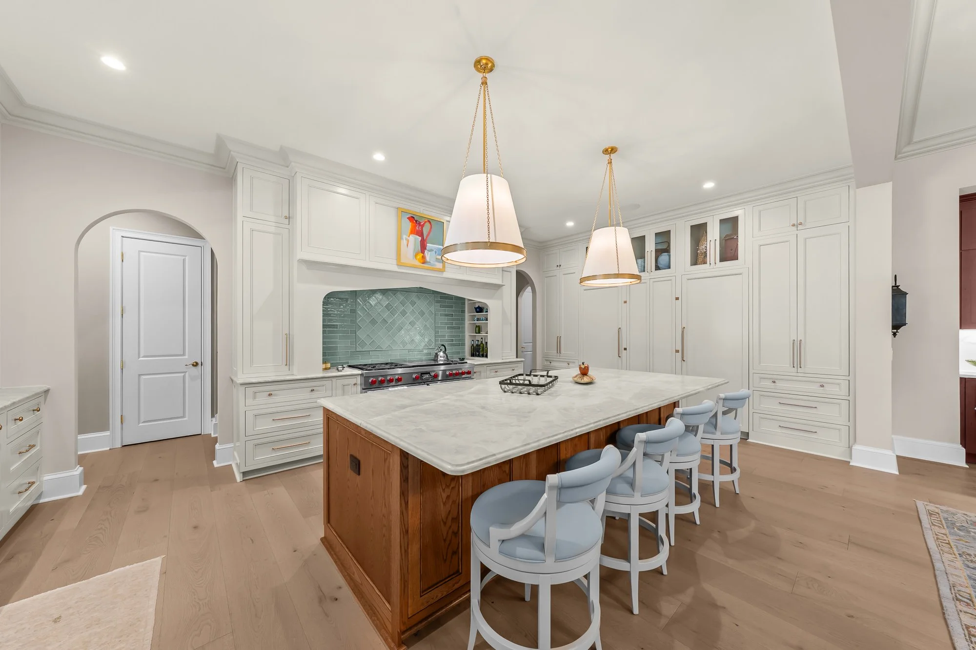 Luxury custom chef's kitchen by FRS Homes featuring an oversized marble island, custom white cabinetry, Wolf range, designer pendant lighting, concealed pantry, and wide-plank hardwood flooring.