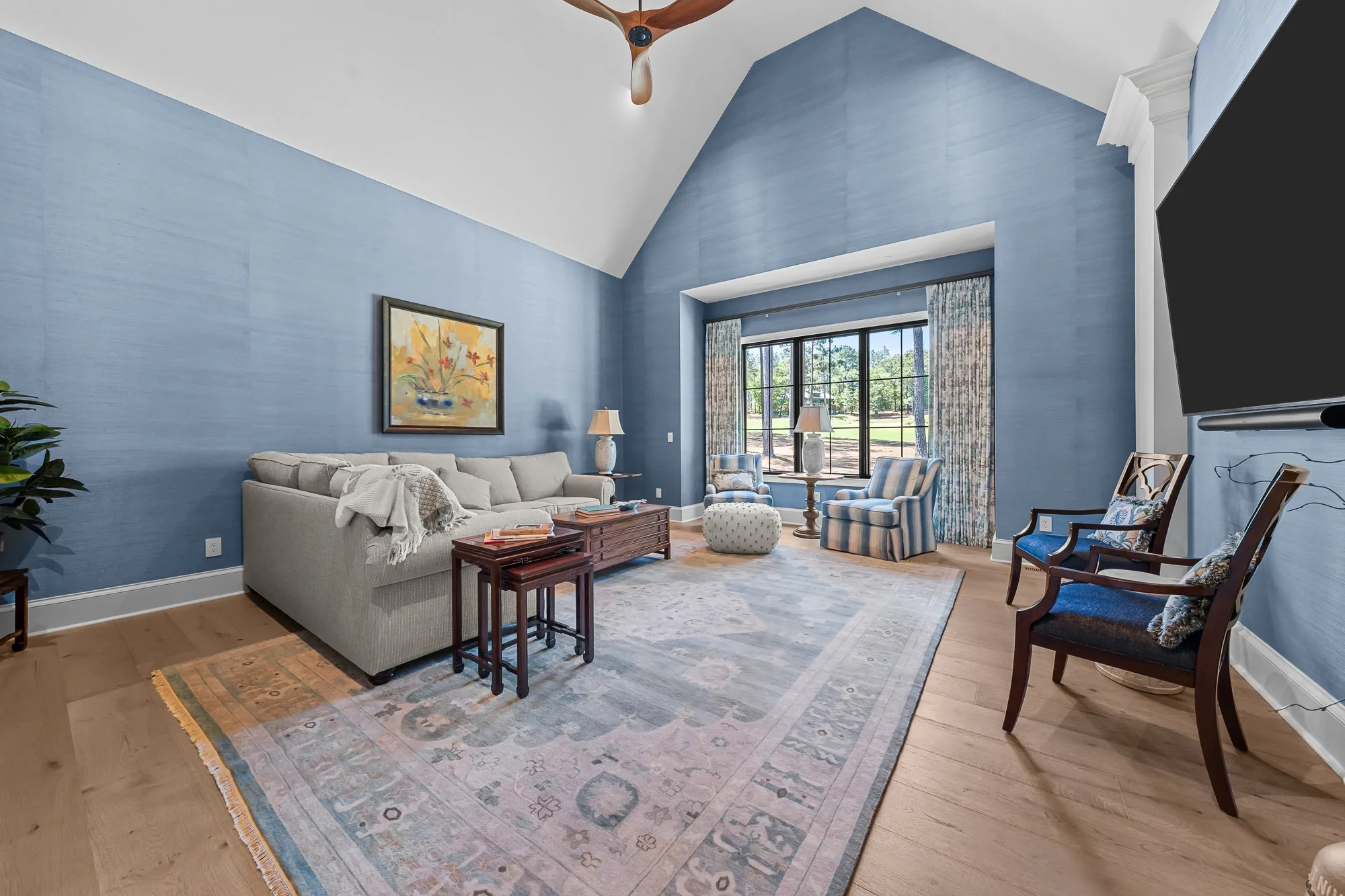 Vaulted bonus room by FRS Homes featuring blue accent walls, hardwood flooring, large picture window, built-in media space, and a comfortable secondary living area.