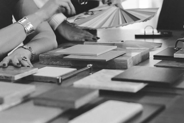 Close-up of hands reviewing material samples, color swatches, and tile options on a table during a custom home design selection process.