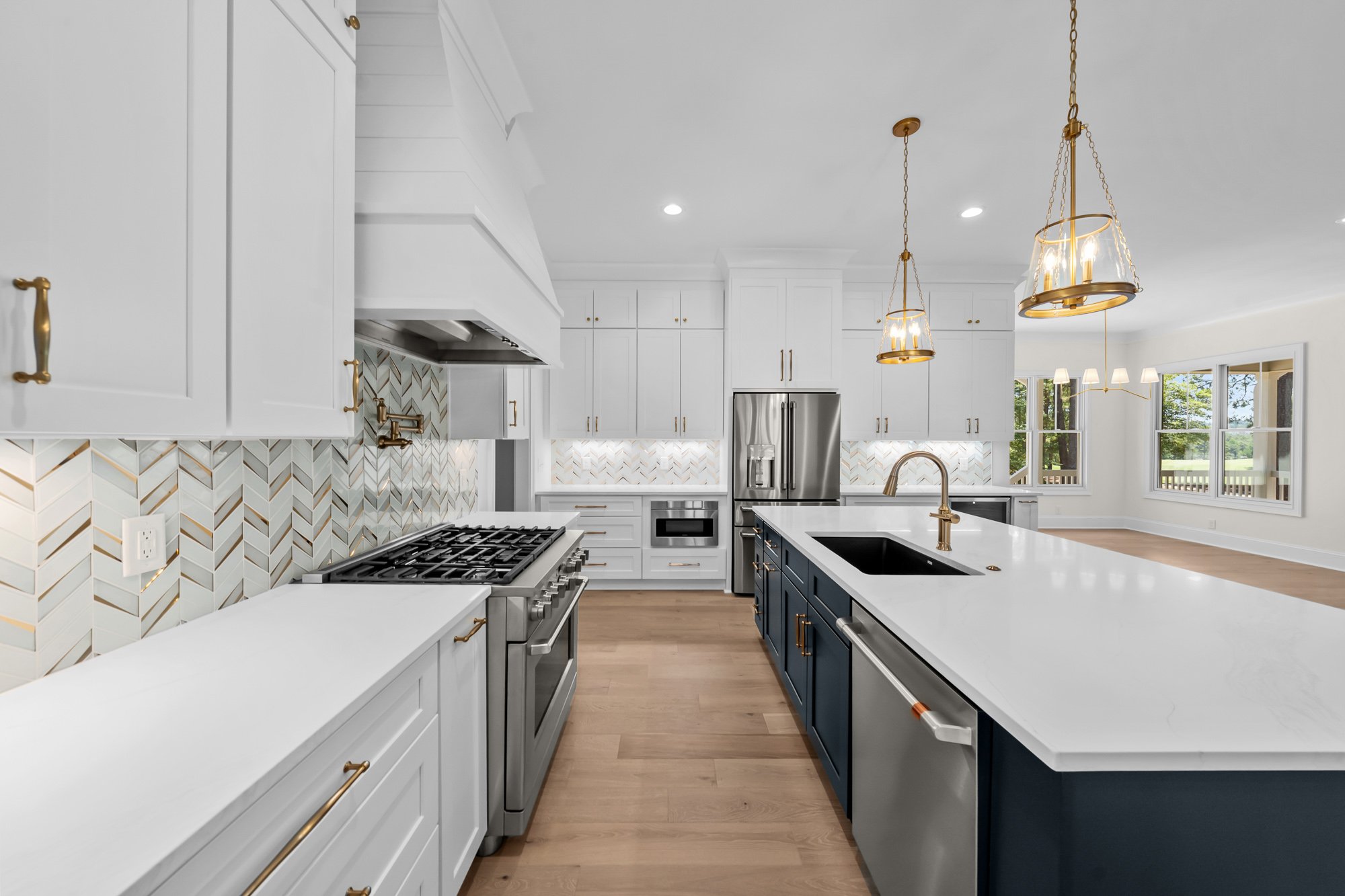 Luxury custom kitchen by FRS Homes featuring white shaker cabinetry, a navy blue island, quartz countertops, designer pendant lighting, and a herringbone tile backsplash.