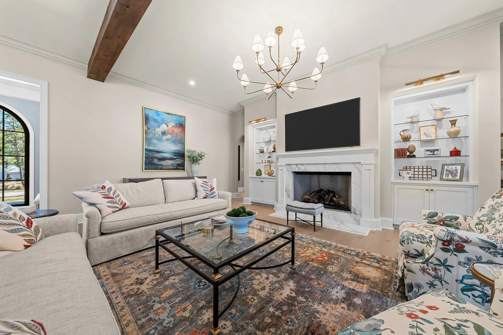 Luxury great room by FRS Homes featuring exposed wood ceiling beams, marble fireplace, custom built-in shelving, designer lighting, and an open-concept living space with hardwood floors.