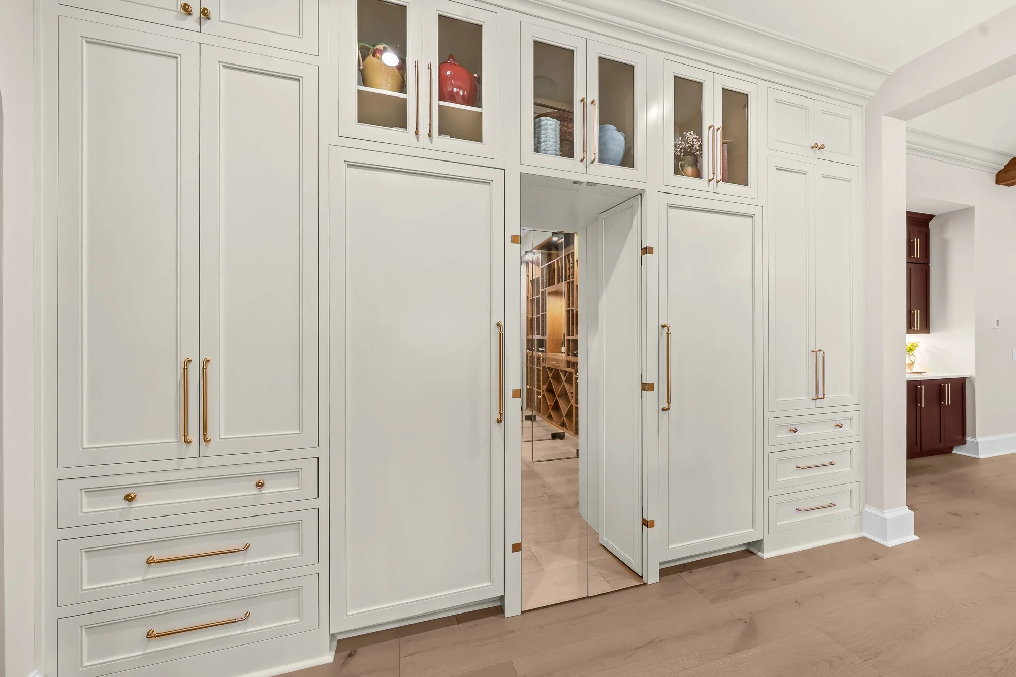 Custom chef's kitchen by FRS Homes featuring floor-to-ceiling white cabinetry with a concealed walk-in pantry entrance leading to a glass-enclosed wine room.