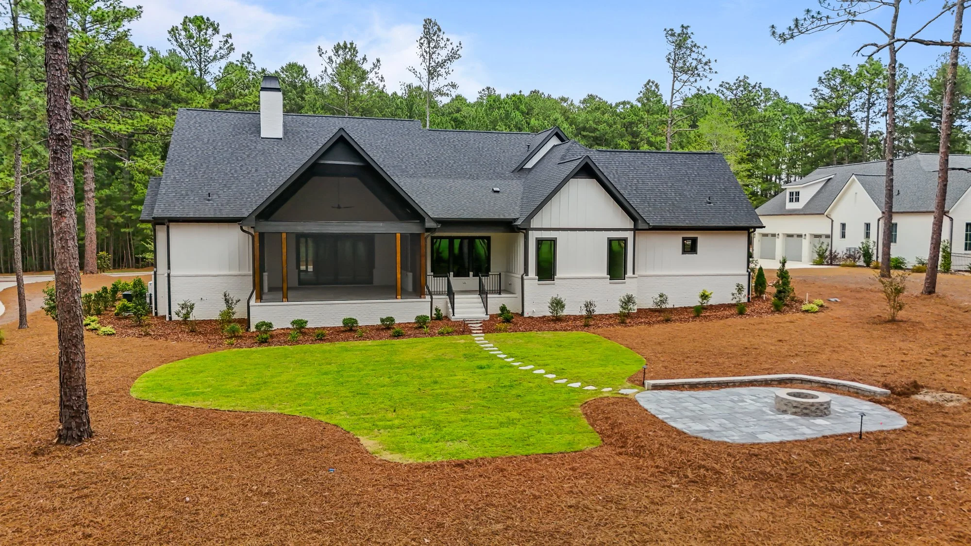 Aerial view of the Foxglove Run custom home showing the screened porch, landscaped backyard, fire pit patio, and surrounding North Carolina pine trees.