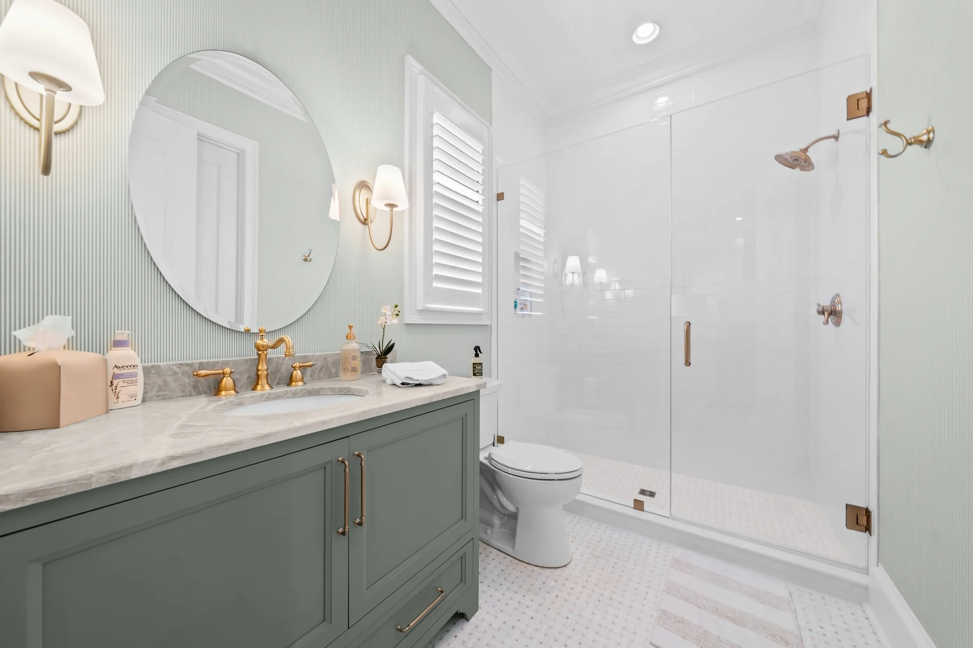 Luxury guest bathroom by FRS Homes featuring a custom green vanity, marble countertop, brass fixtures, frameless glass shower, and bright timeless finishes.