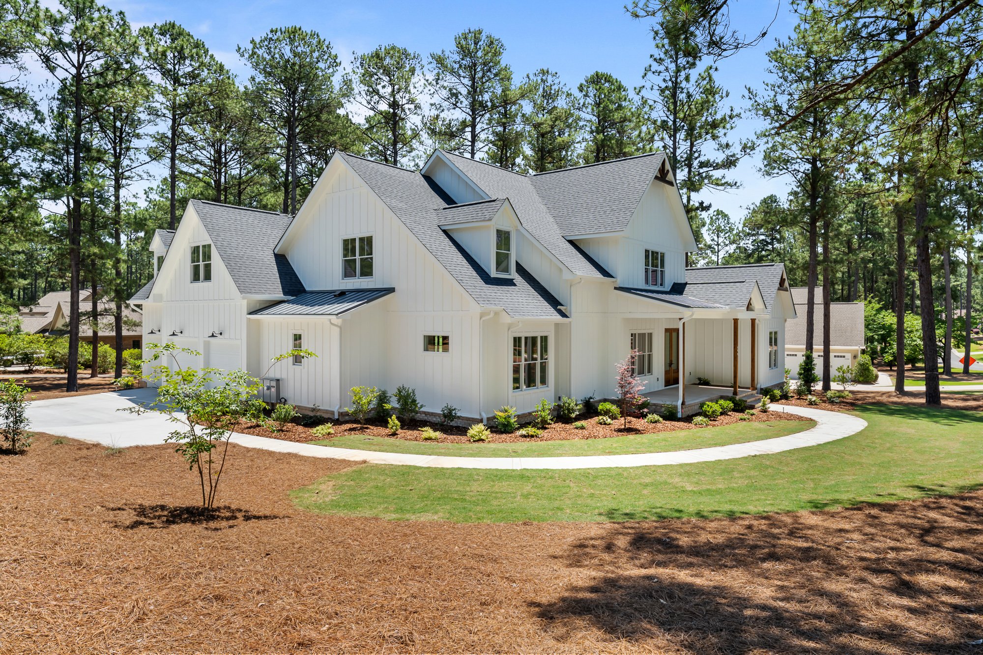 Custom white farmhouse exterior by FRS Homes featuring board and batten siding, multiple gables, landscaped grounds, and a curved concrete walkway.