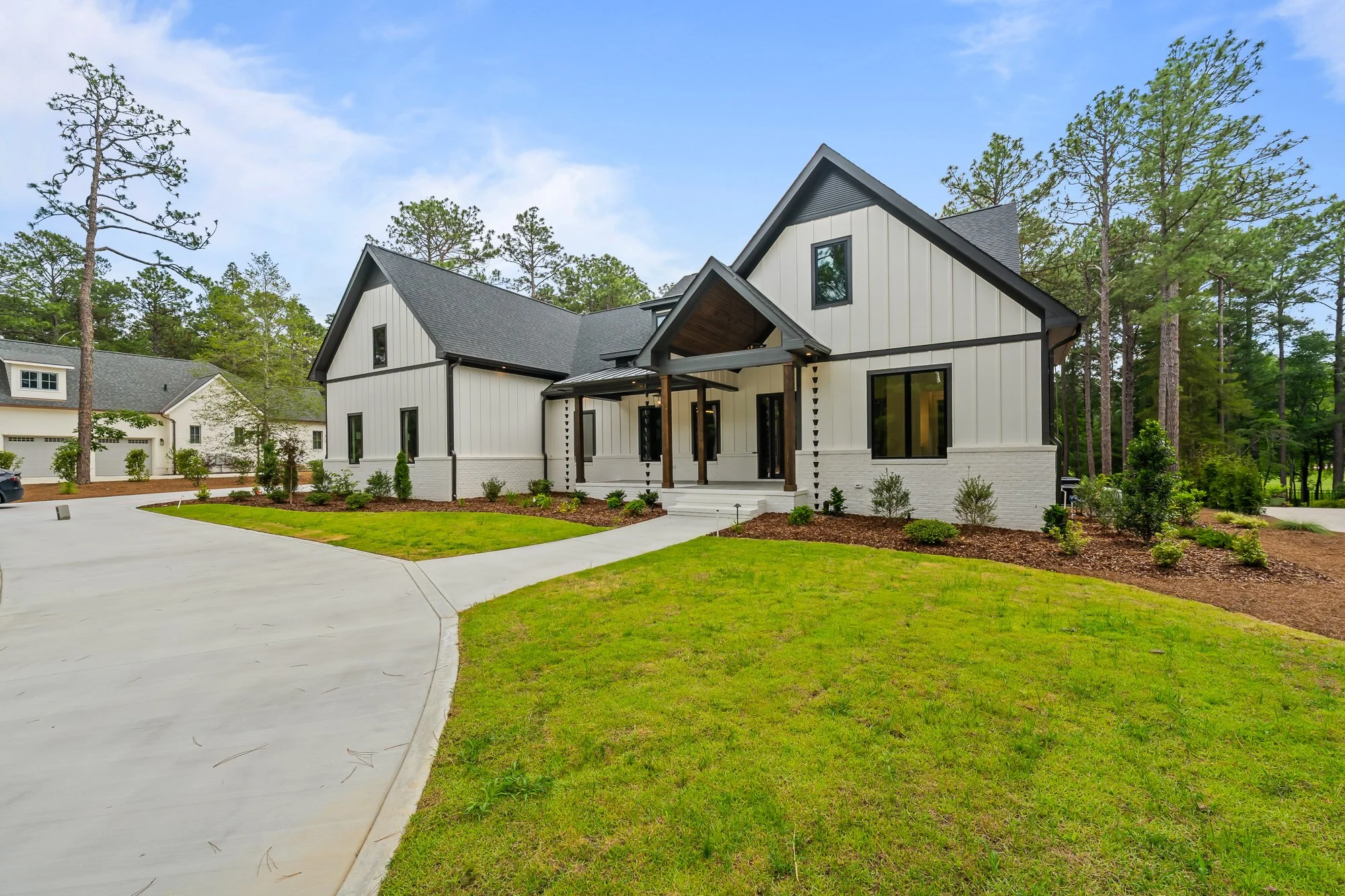 Angled view of Foxglove Run showcasing modern farmhouse architecture, white siding, black-framed windows, natural wood accents, and landscaped grounds.