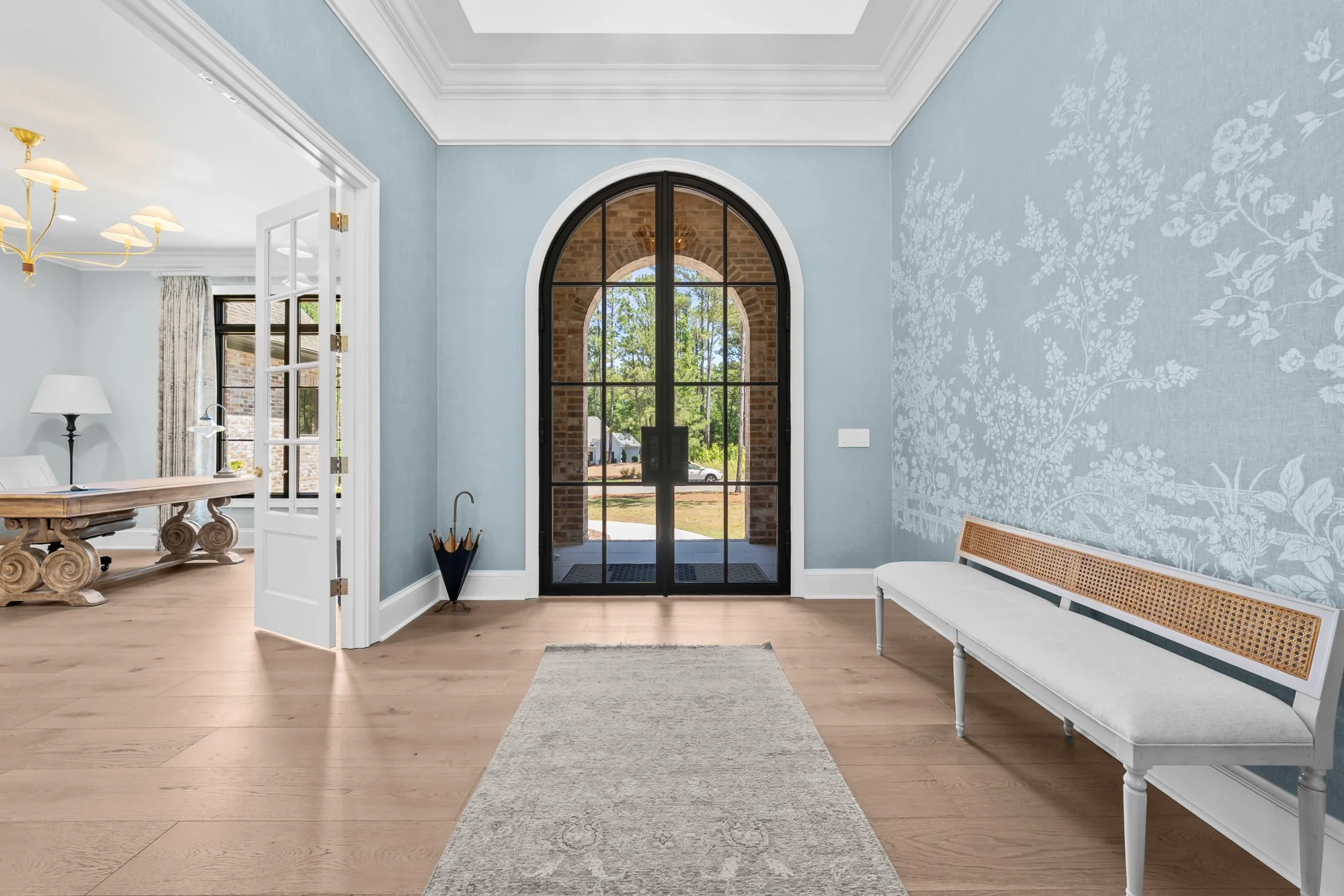 Luxury foyer by FRS Homes featuring an arched black steel front door, designer blue wallcovering, tray ceiling, hardwood floors, and a bright, welcoming entryway.