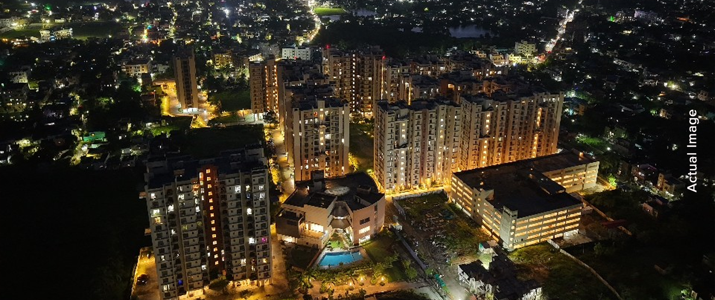 Modern apartment buildings with glass exteriors, surrounded by palm trees and a small pond, under a clear blue sky.