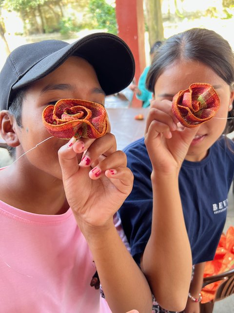 Two young women holding colorful fabric rosettes in front of their eyes