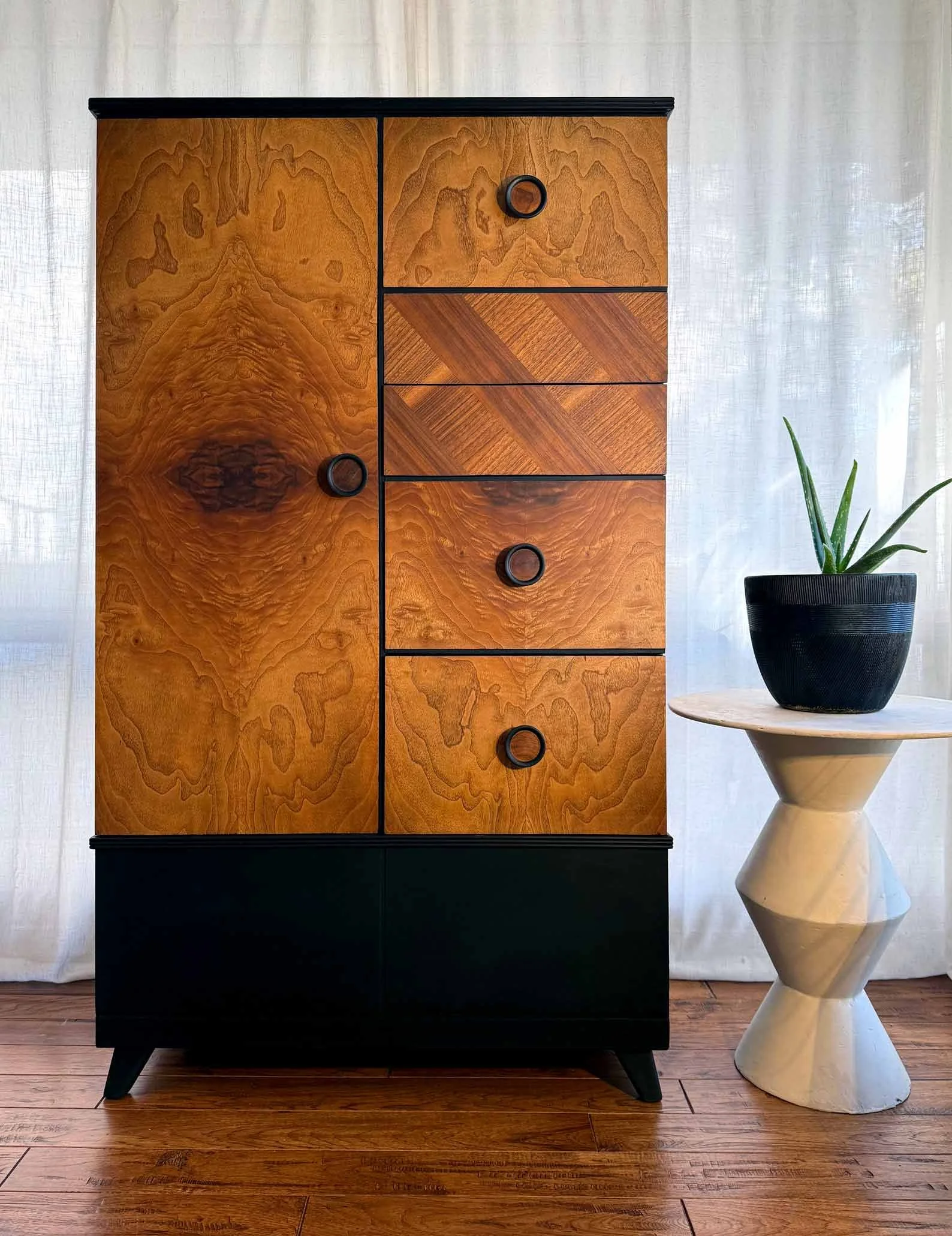 A wooden armoire, or chifferobe, with a combination of natural wood grain details and black accents. A hybrid piece with both drawers and a cabinet component to make the experience of storing your clothes feel both seamless and sophisticated.