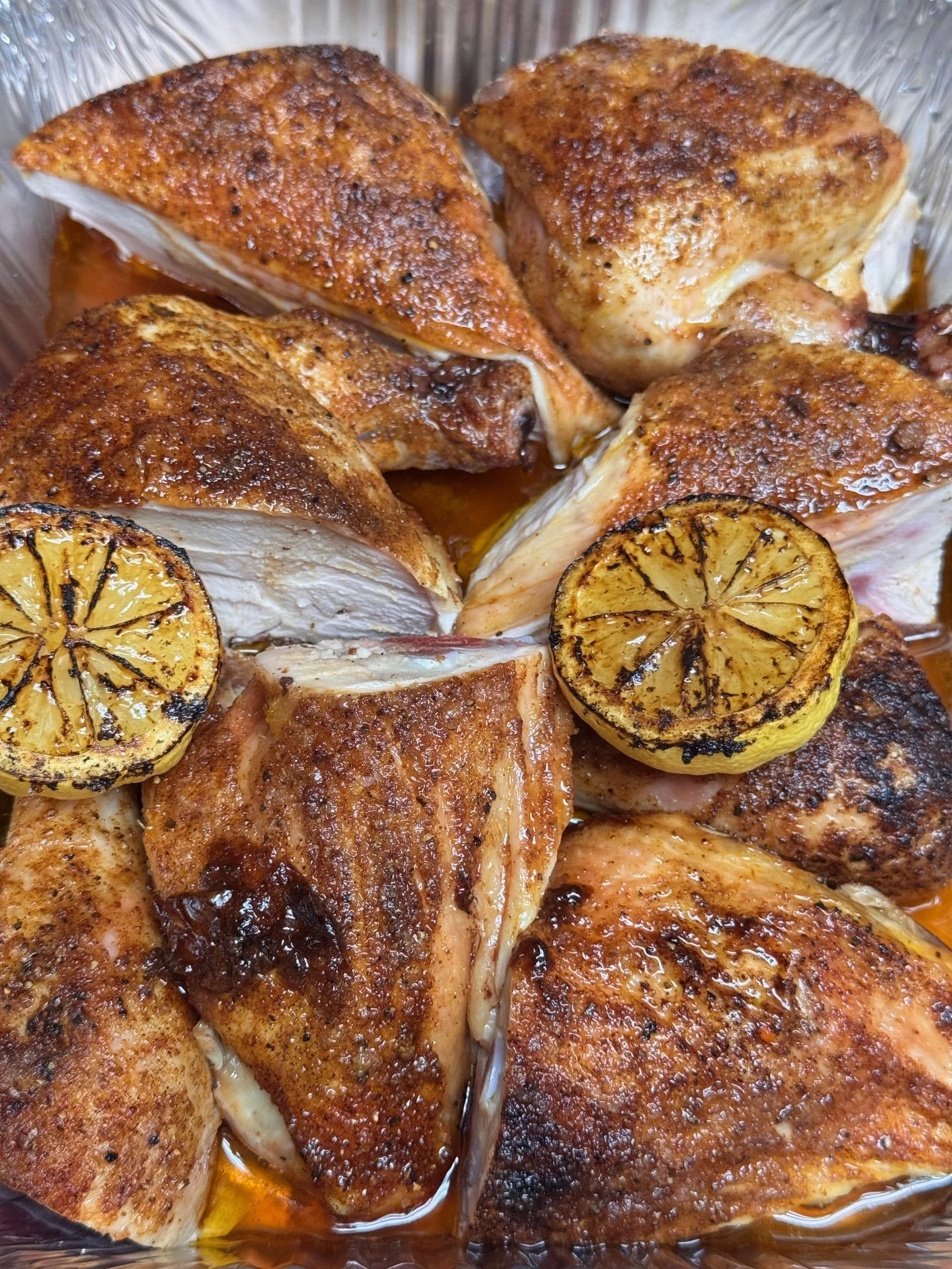 Four seasoned chicken thighs with grilled lemon slices in a baking dish.