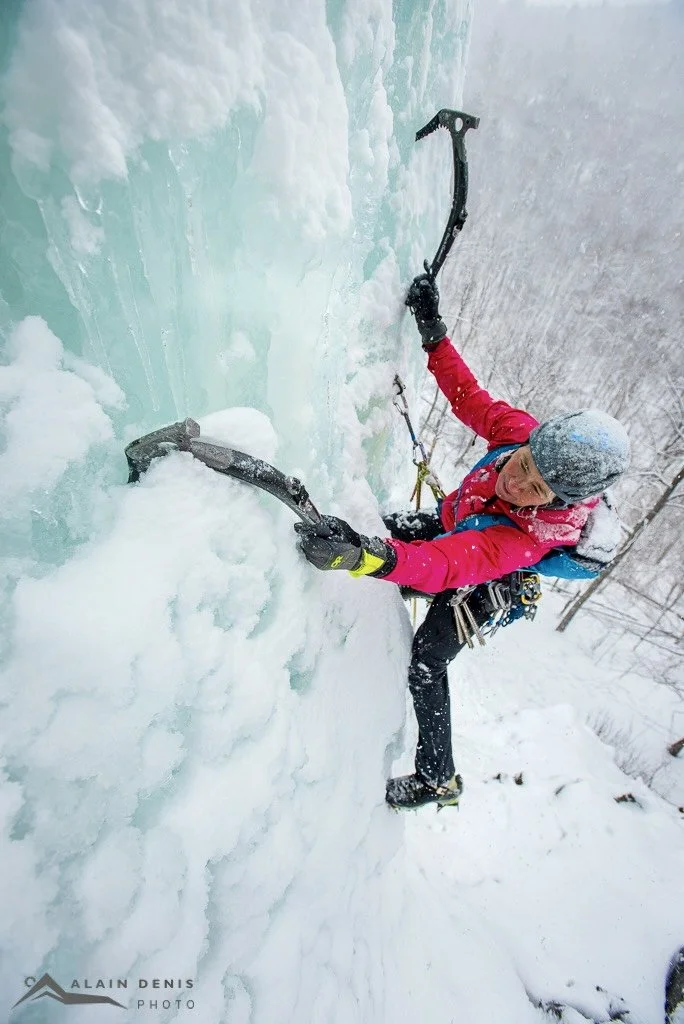 women lead climbing a frozen water fall with black diamond ice tools, a pink jacket, and a grey helmet