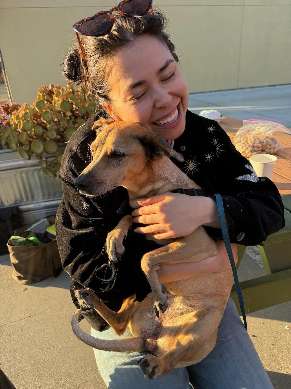 woman smiling and hugging a small tan dog